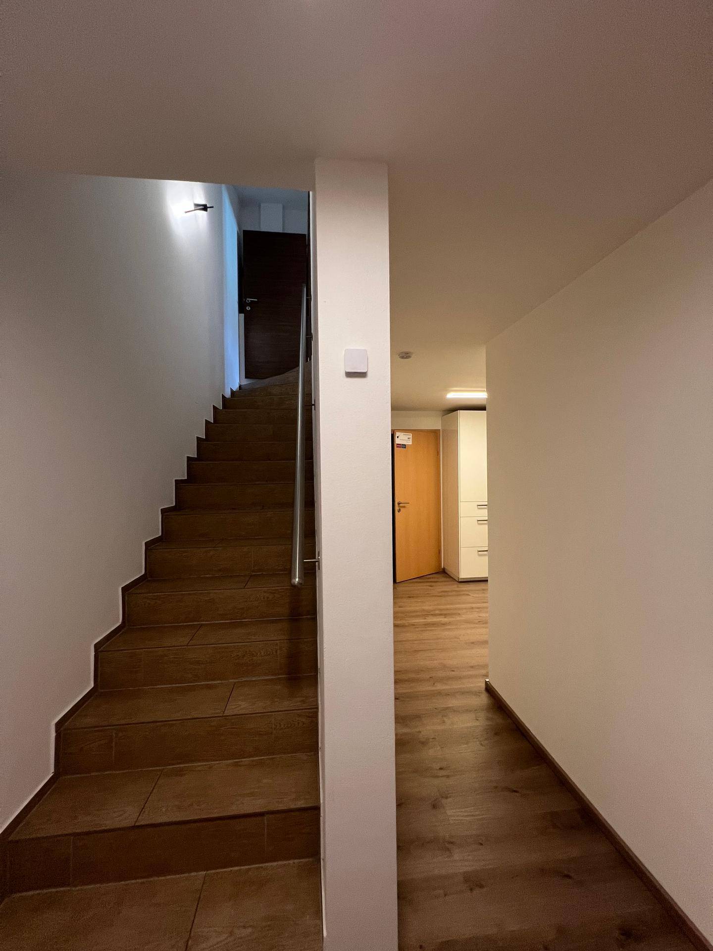 Heller Flur mit Treppenaufgang zum Obergeschoss und Holzoptik-Fliesenboden.