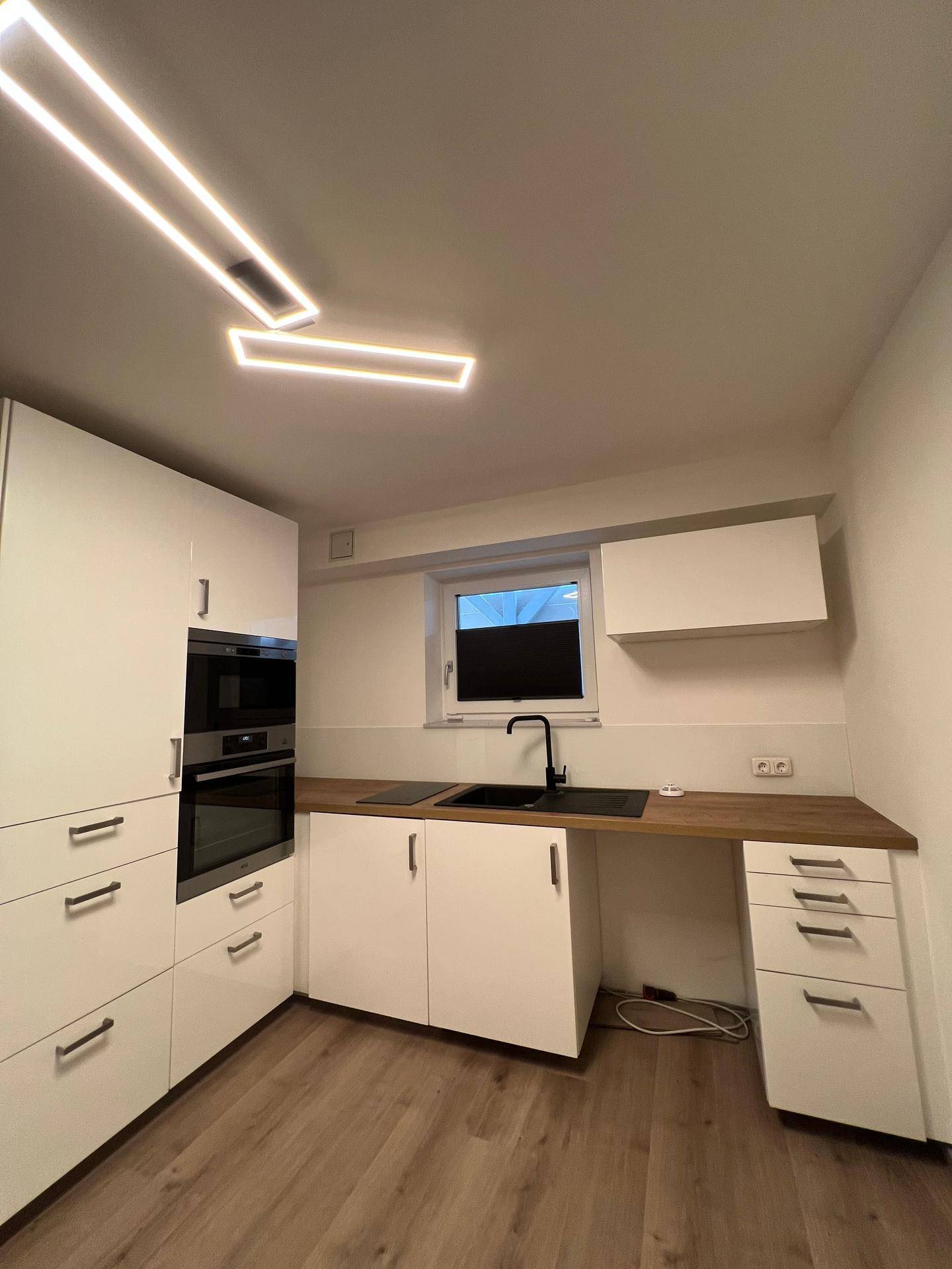Kompakte Küche mit weißen Schränken, Holz-Arbeitsplatte und modernen Leuchten.