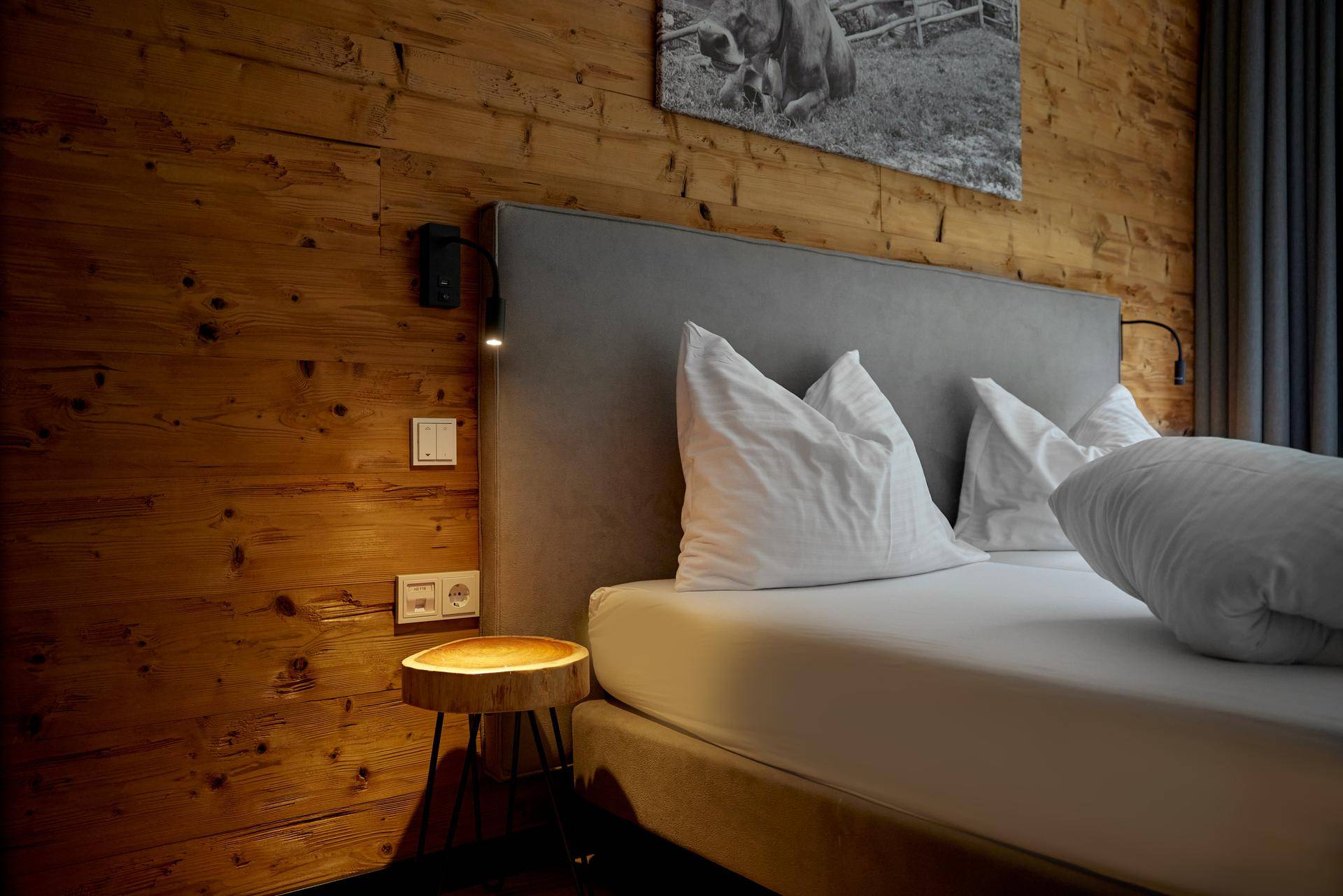 Detailansicht des Bettes in einem Schlafzimmer mit rustikaler Holzwand und modernem Nachttisch.