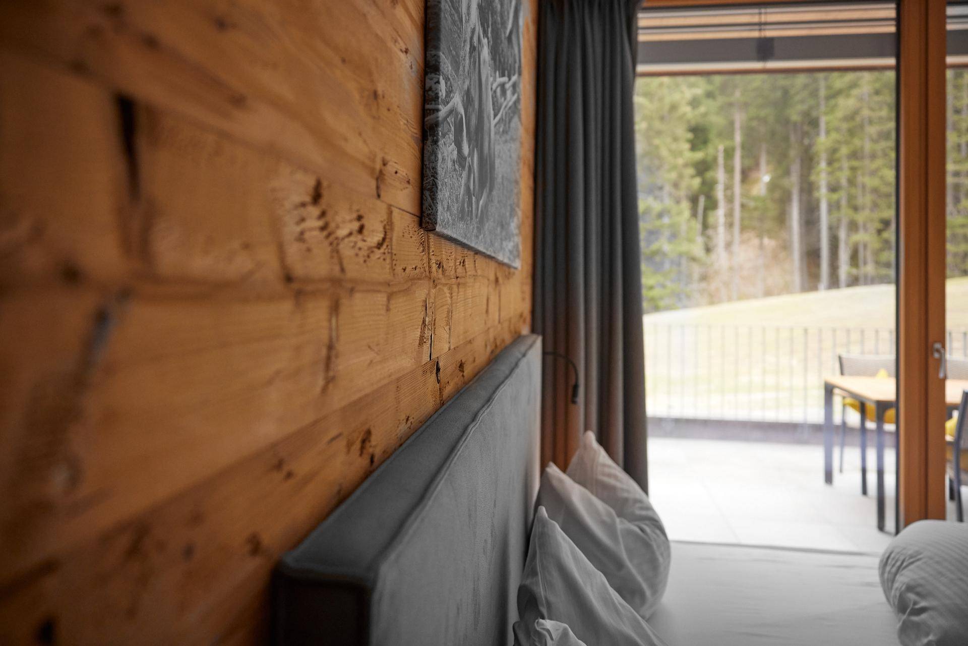 Schlafzimmer mit Holzwand, Vorhängen und Blick auf die grüne Umgebung von der Terrasse.
