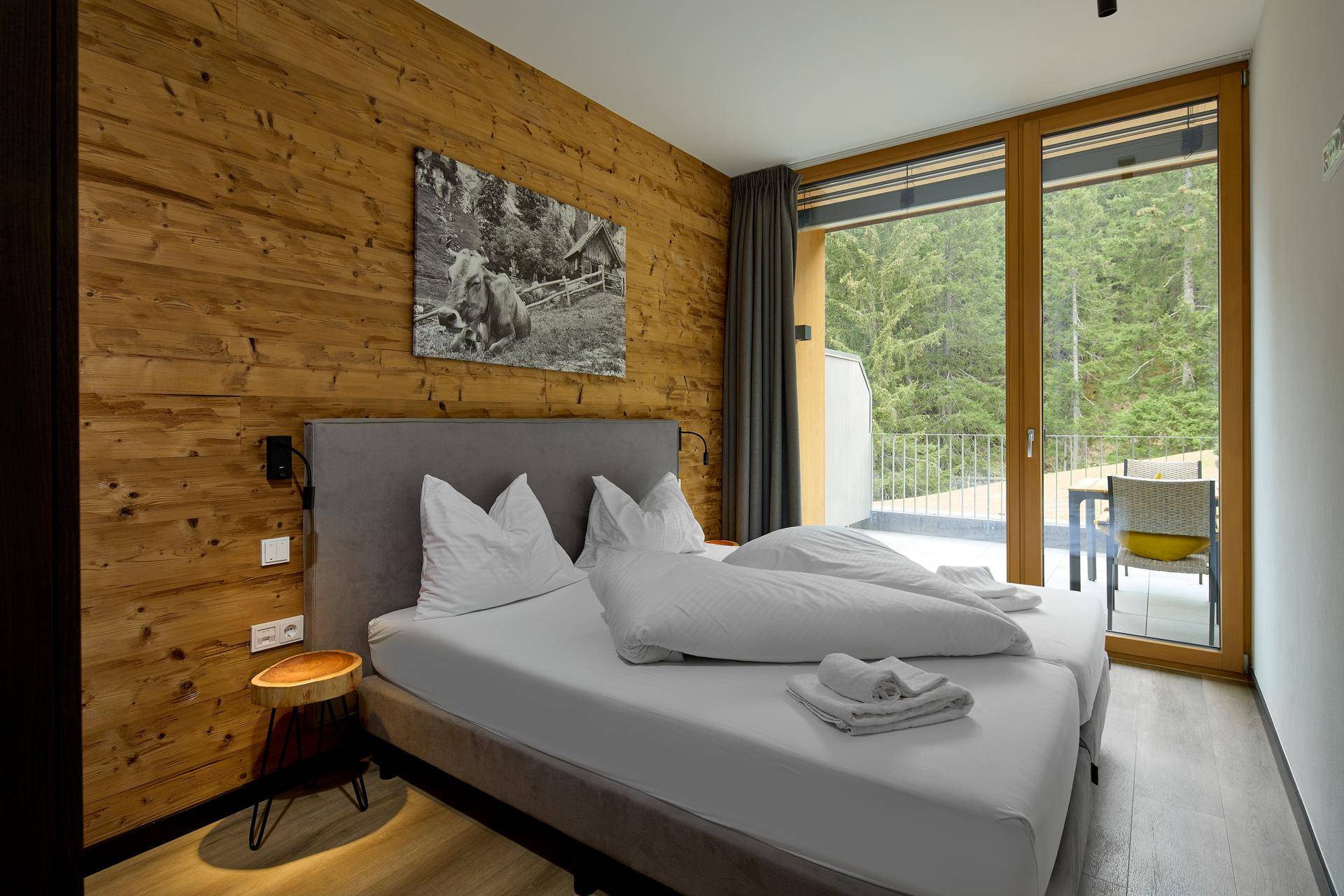 Gemütliches Schlafzimmer mit Holzwandverkleidung, Doppelbett und direktem Zugang zur Terrasse mit Waldblick.