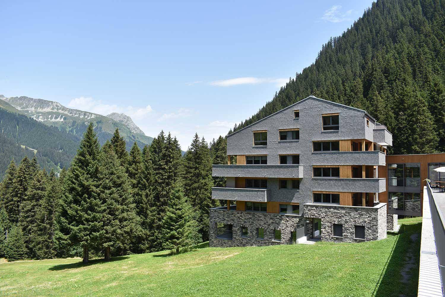 Modernes Gebäude mit Stein- und Holzfassade, eingebettet in die alpine Waldlandschaft.