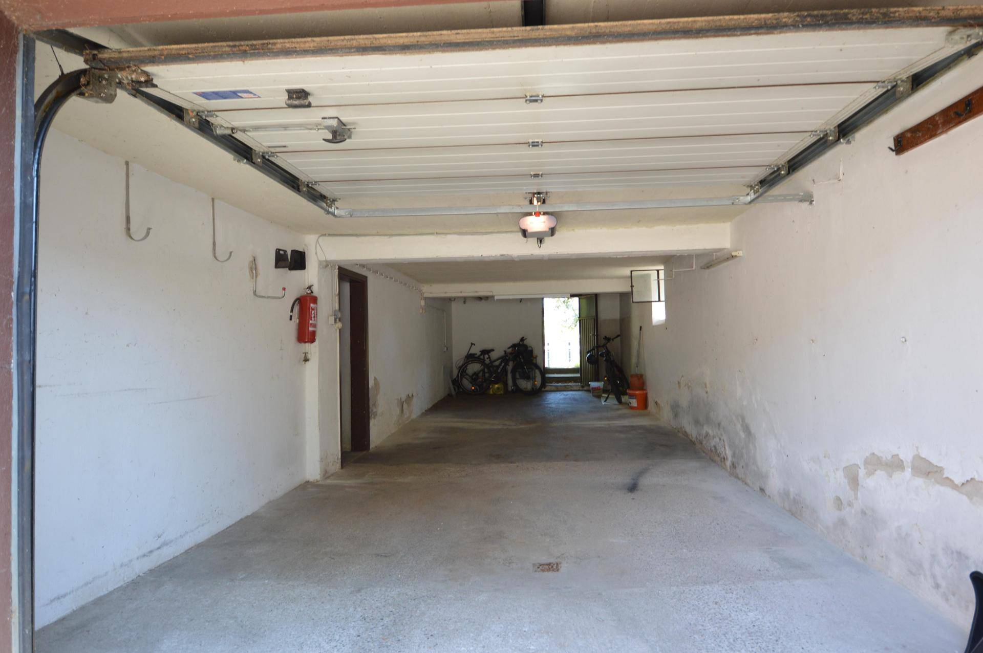 Geräumige Garage mit offenem Tor, Betonboden und Platz für Fahrräder und Abstellmöglichkeiten.