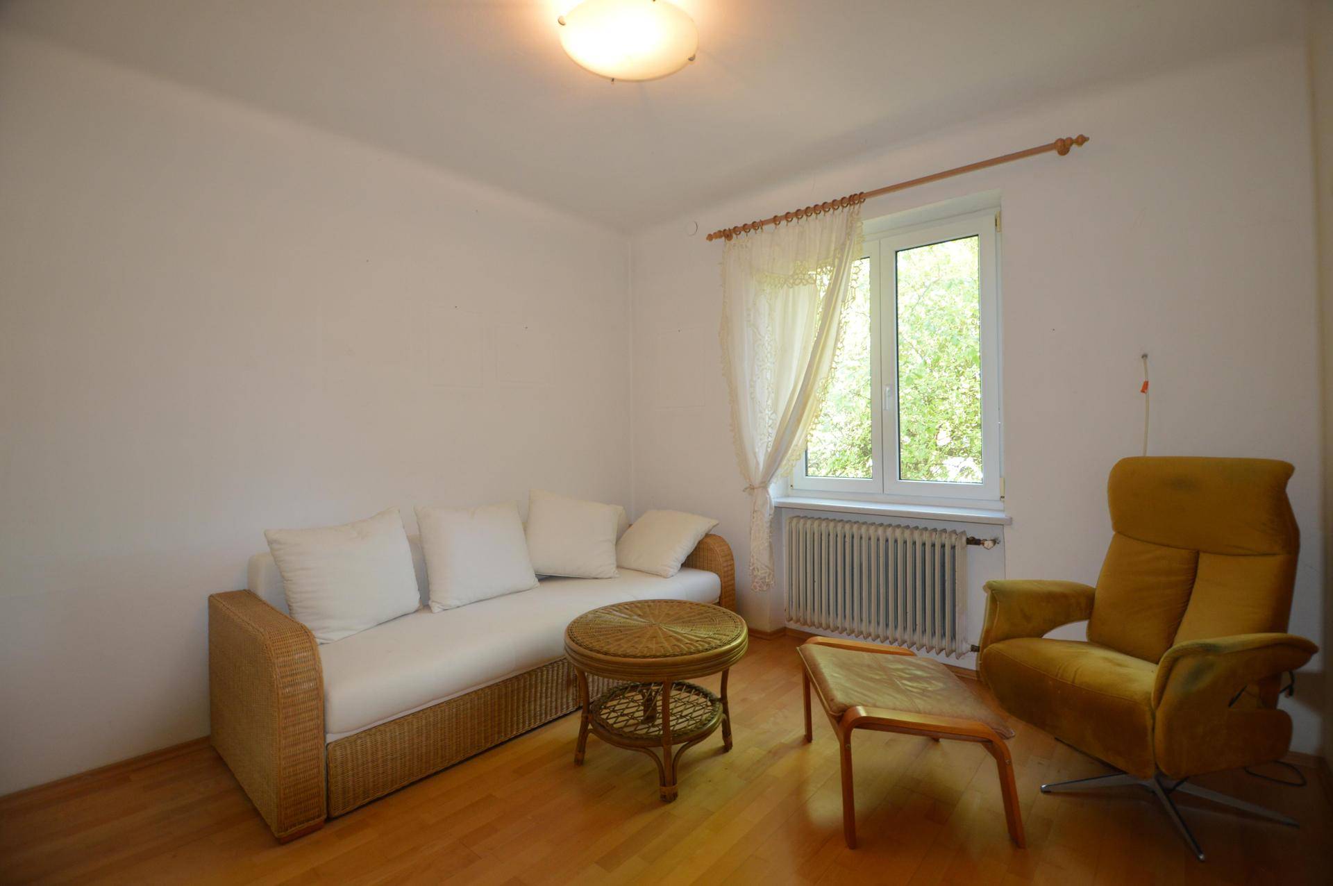 Helles Wohnzimmer mit Parkettboden, einem Sofa aus Rattan und einem Sessel in Senfgelb.