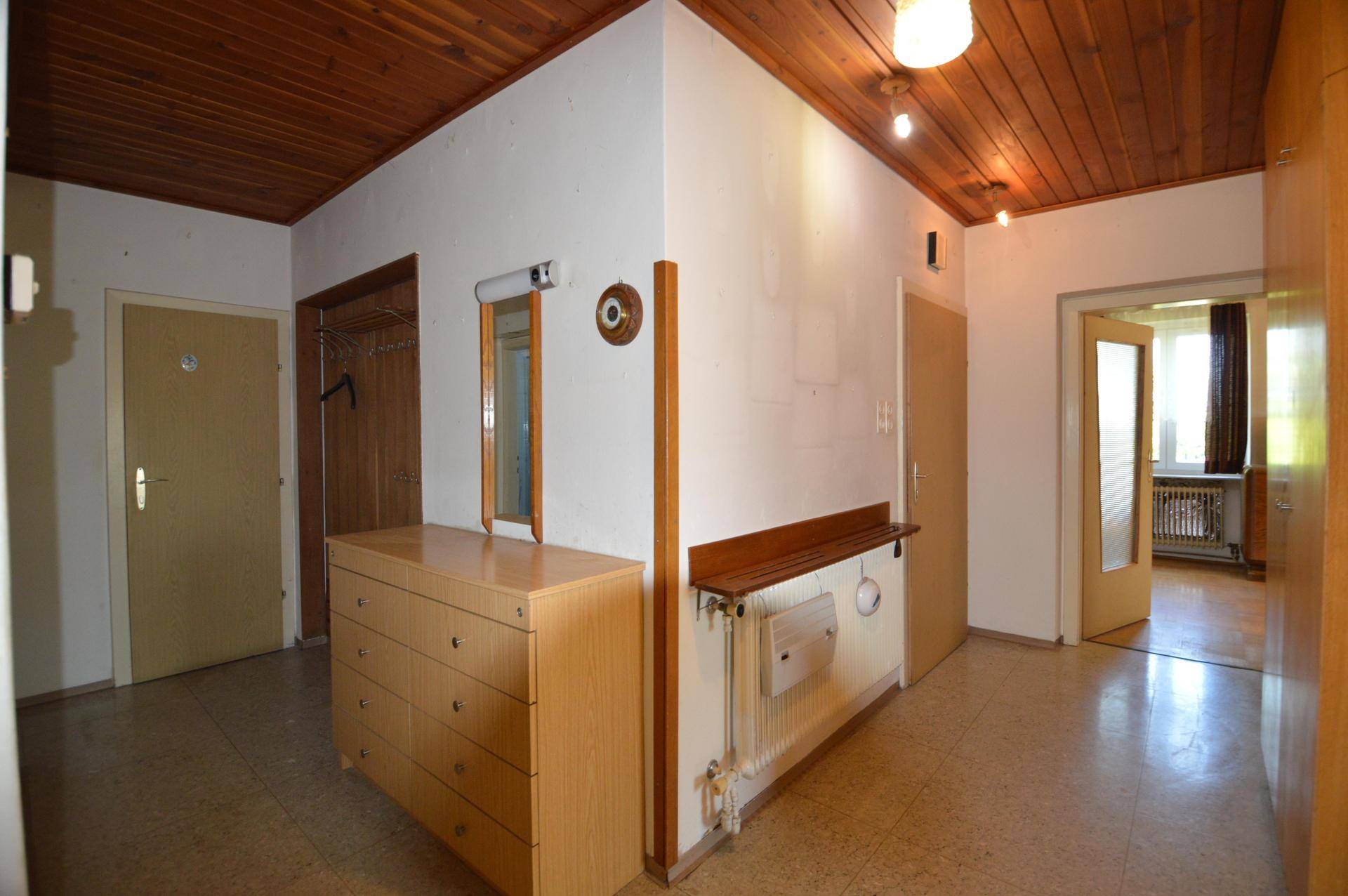 Flur mit Holzdecke, Fliesenboden und einer Kommode mit Spiegel in warmen Holztönen.