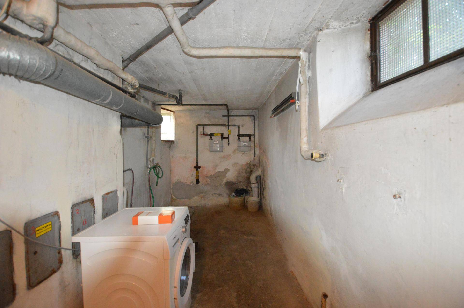 Waschküche im Keller mit Waschmaschine, Versorgungsleitungen und kleinem Fenster für Belüftung.