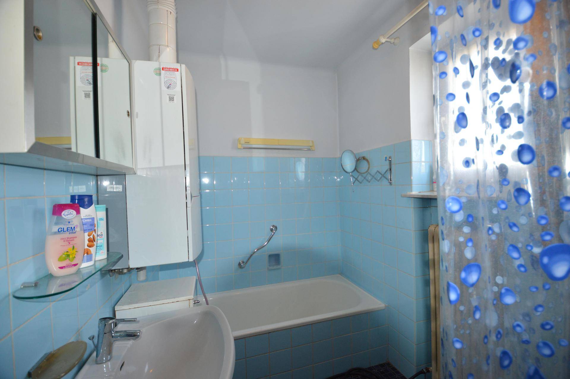 Badezimmer mit blauen Fliesen, Badewanne, Waschbecken und einem Spiegelschrank.