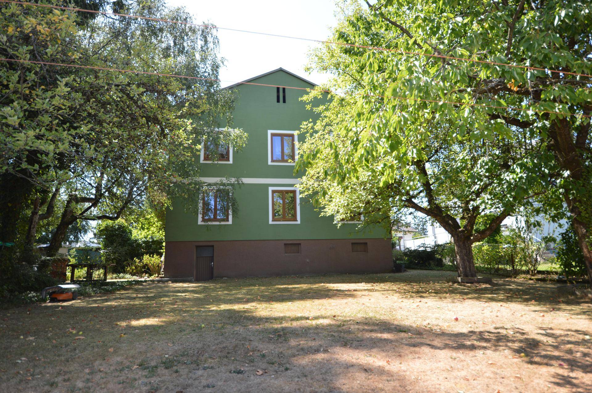 Rückansicht des Hauses mit grün gestrichener Fassade und großem Rasenbereich umgeben von Bäumen.
