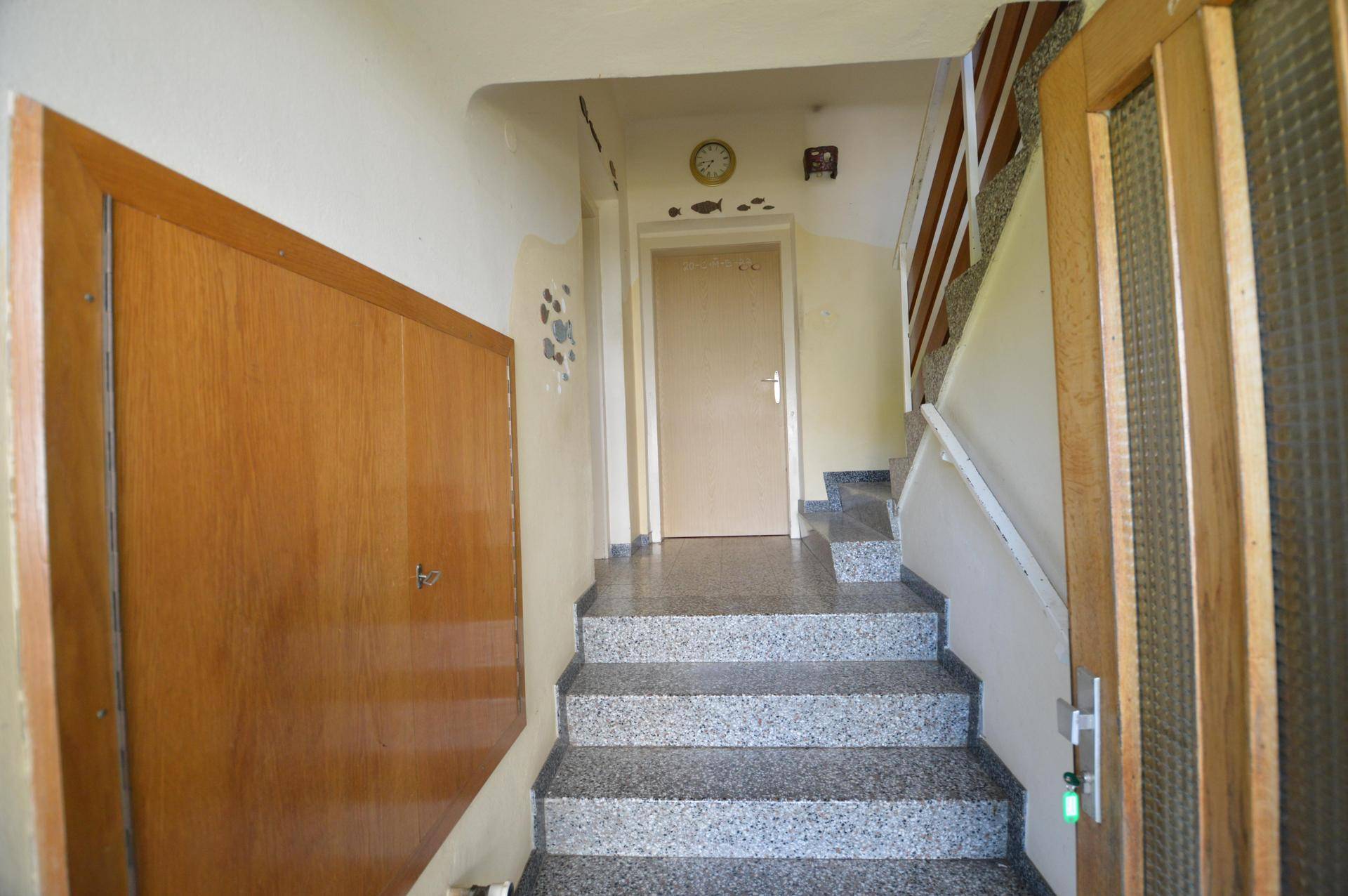 Eingangsbereich mit Treppe, Terrazzoboden und einer Holzverkleidung an der Wand.