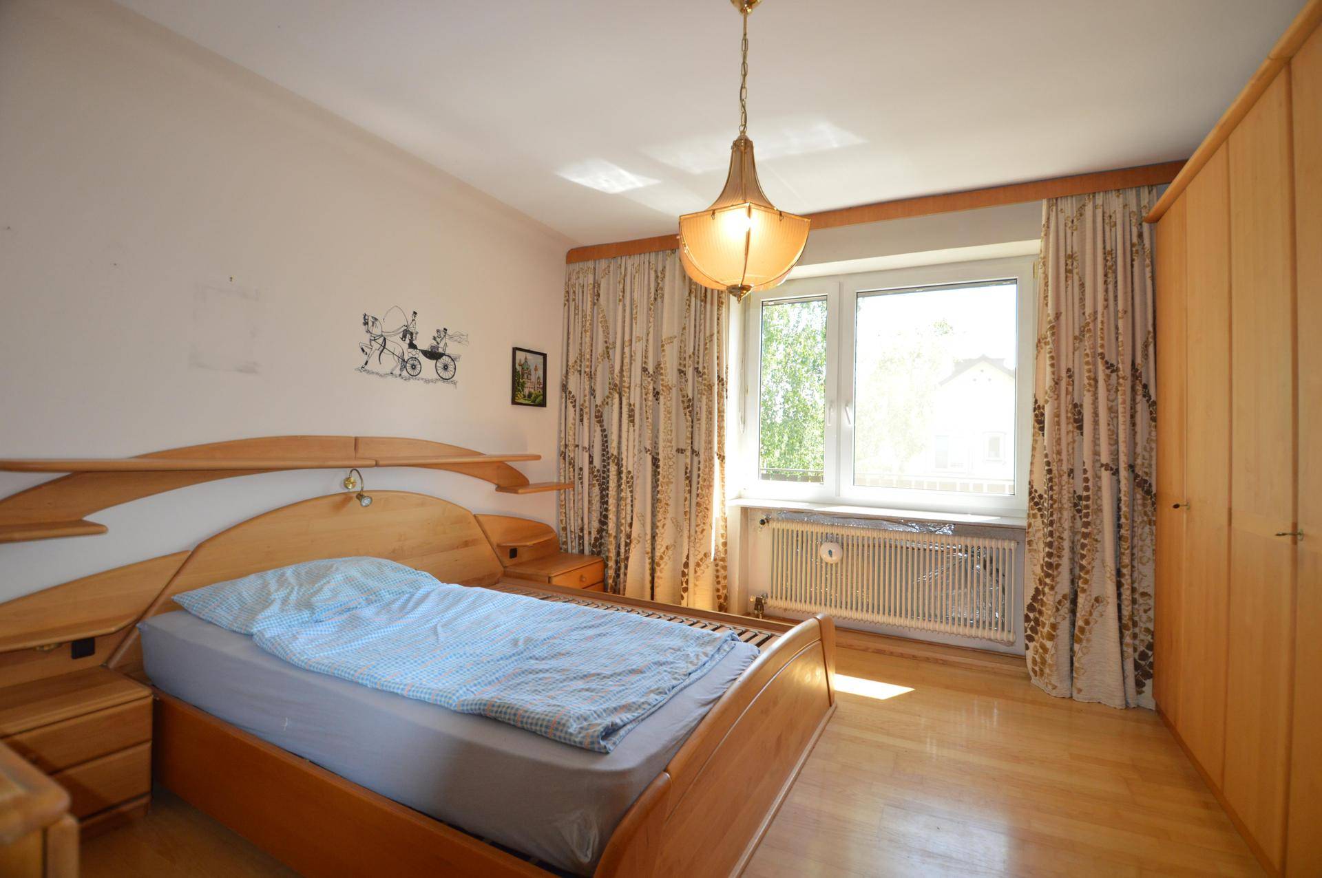 Schlafzimmer mit Holzbett, Parkettboden und einem Fenster, das viel natürliches Licht hereinlässt.