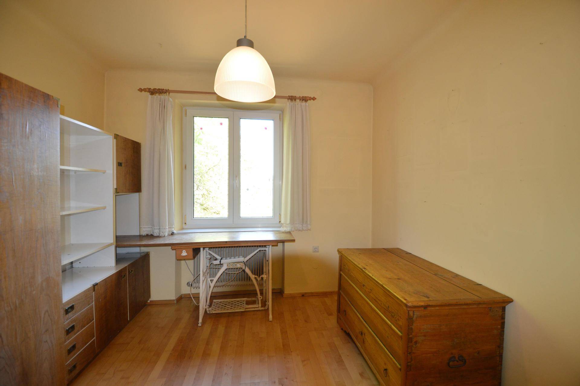 Zimmer mit hellem Holzboden, einem Schreibtisch an der Fensterfront und einer antiken Holzkommode.