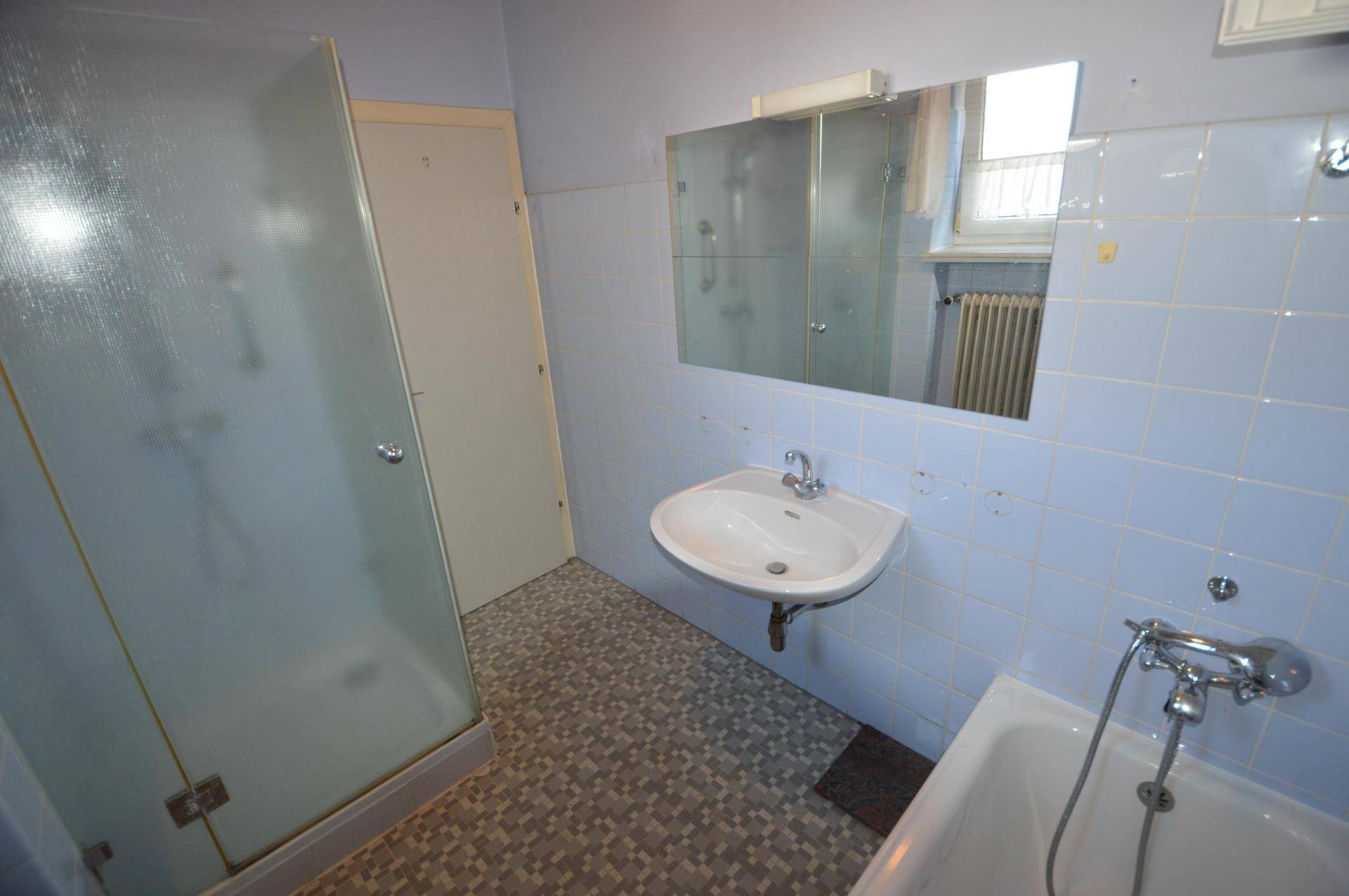 Badezimmer mit blauen Fliesen, Badewanne, Duschkabine und einem Waschbecken mit Spiegel.