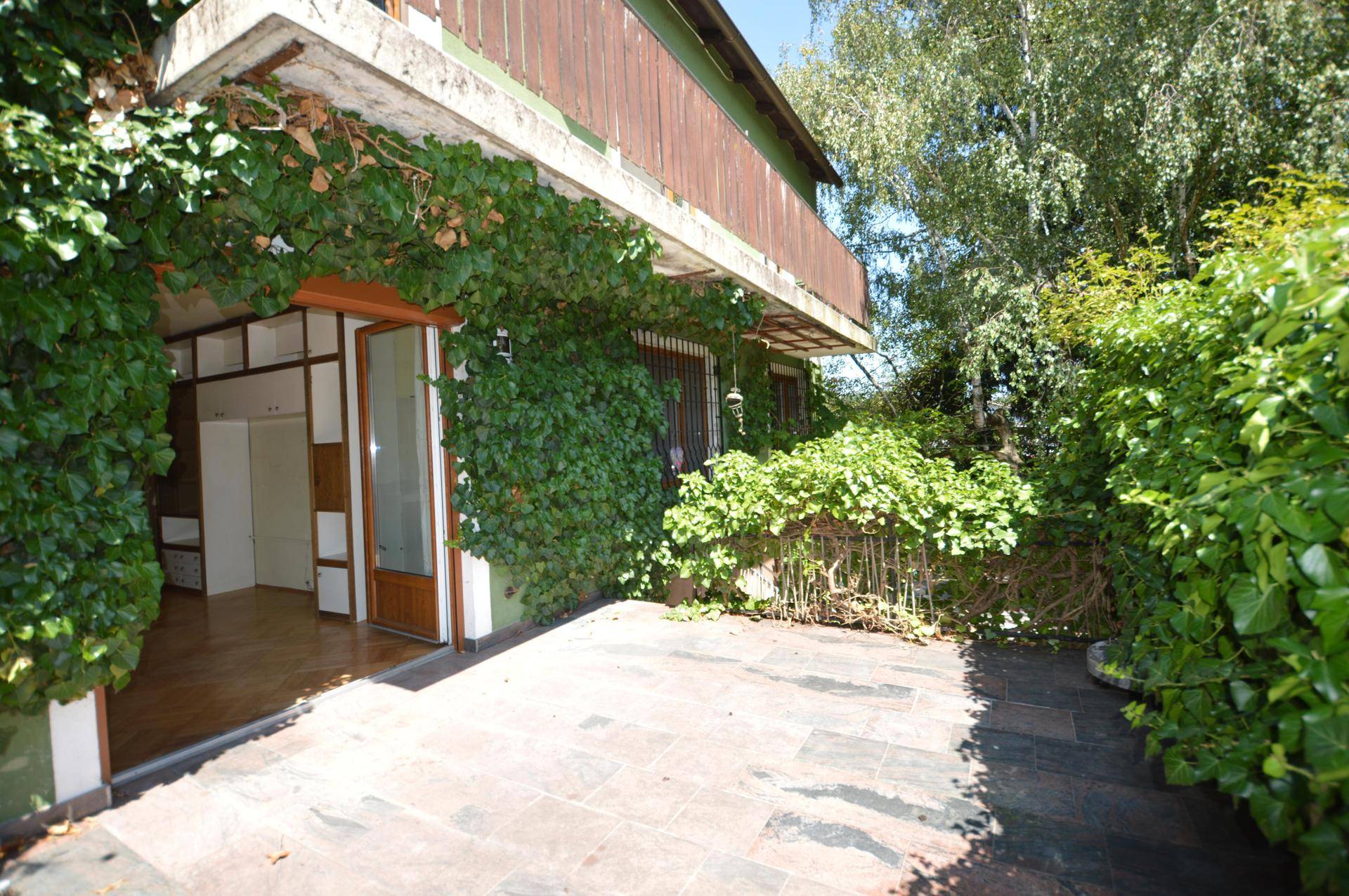 Gepflasterte Terrasse mit üppiger Begrünung und direktem Zugang zum Innenbereich des Hauses.