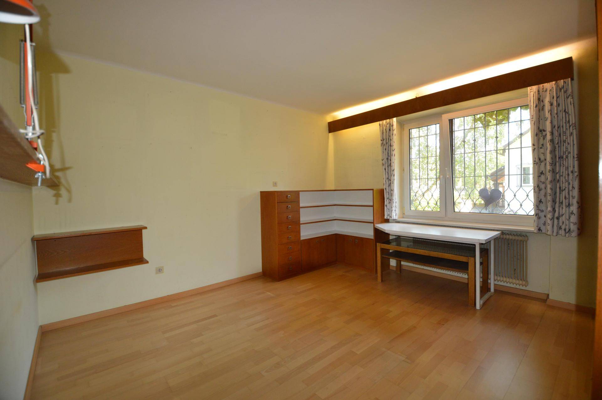 Zimmer mit hellem Holzboden, Einbauregalen und einem Fenster mit Blick auf die grüne Umgebung.