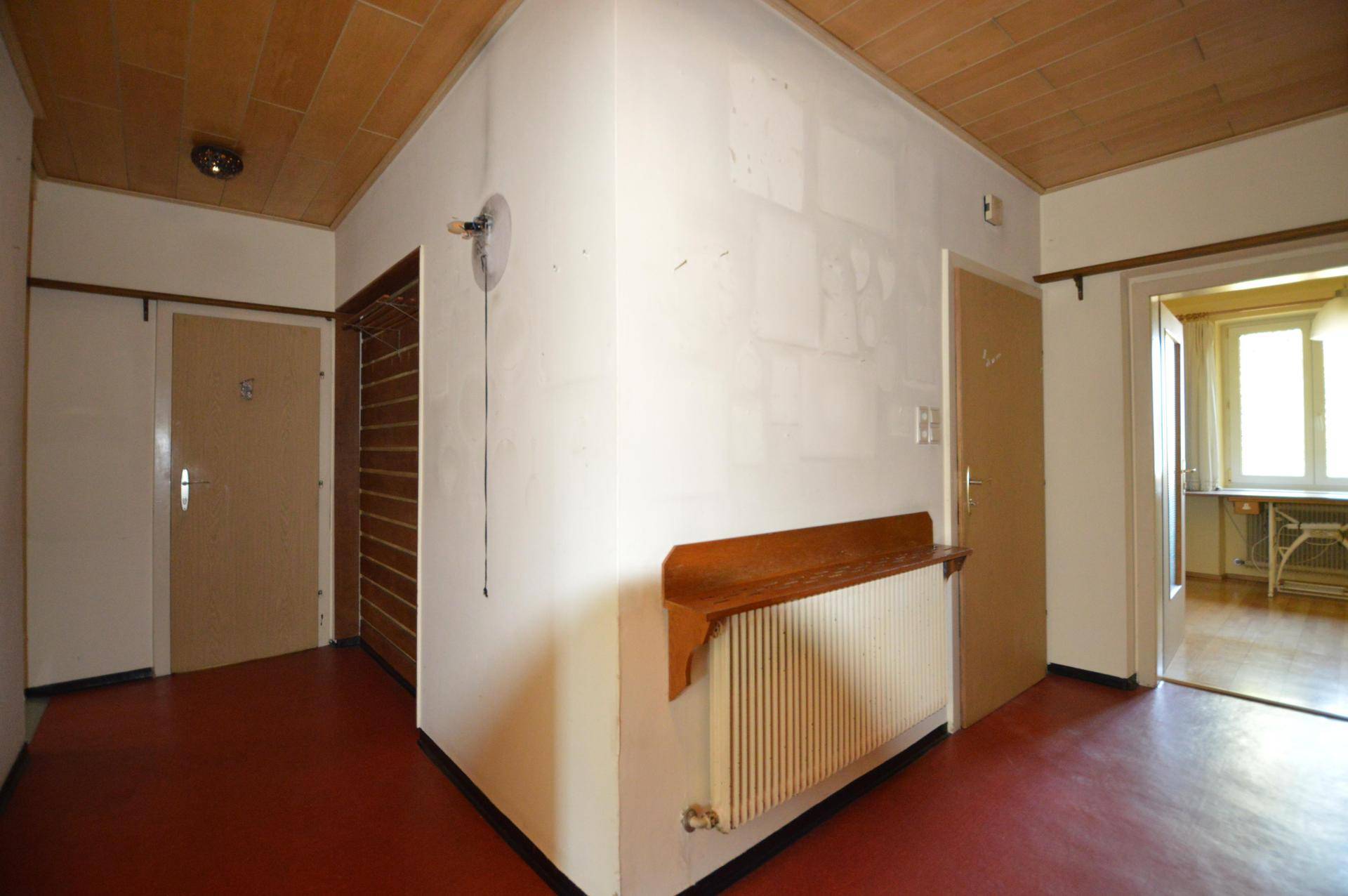 Flur mit Holzdecke, rotem Linoleumboden und einem Heizkörper mit Holzablage.