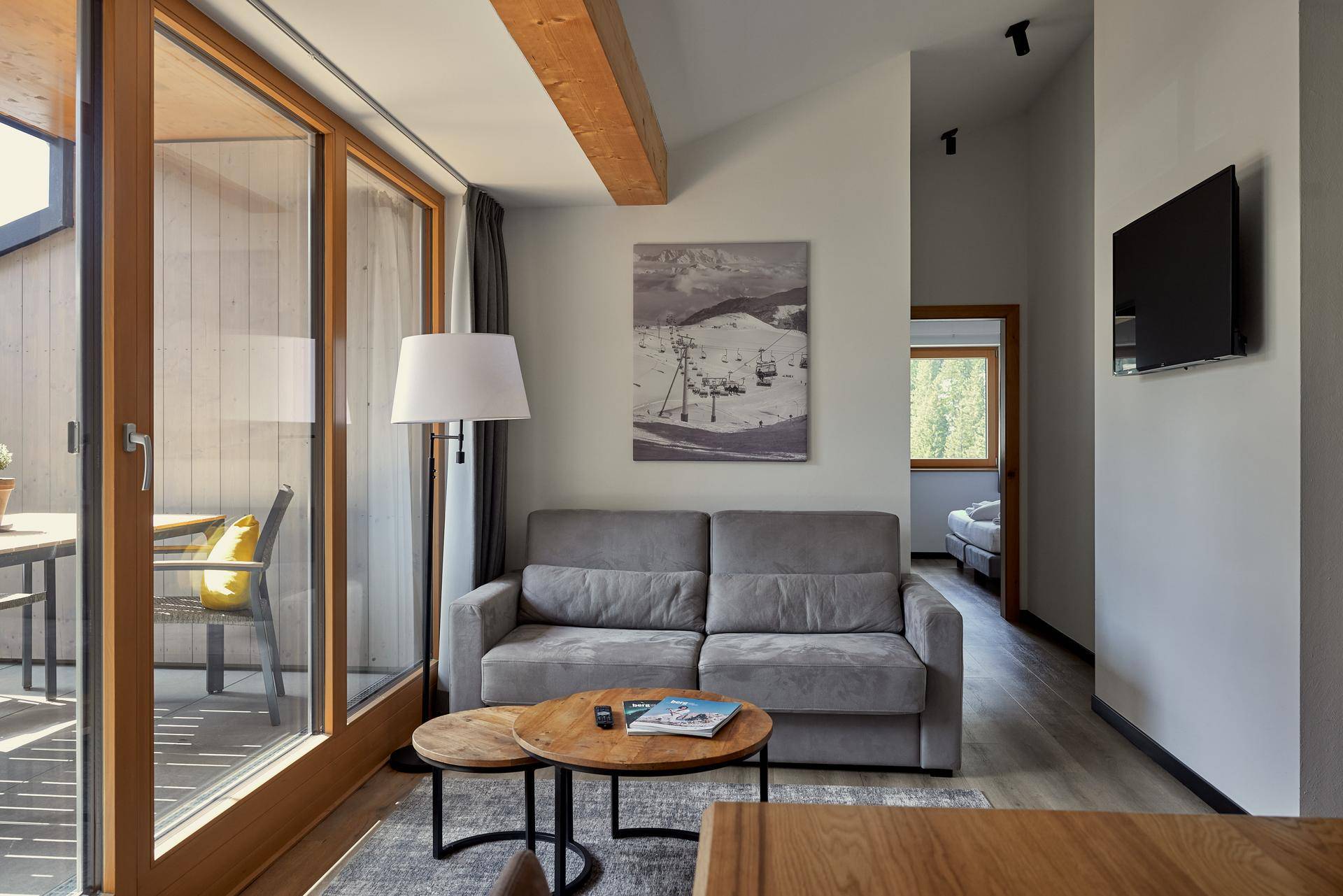 Wohnzimmer mit Sofa, Couchtisch und Zugang zu einem weiteren Raum, mit Bergbild an der Wand.