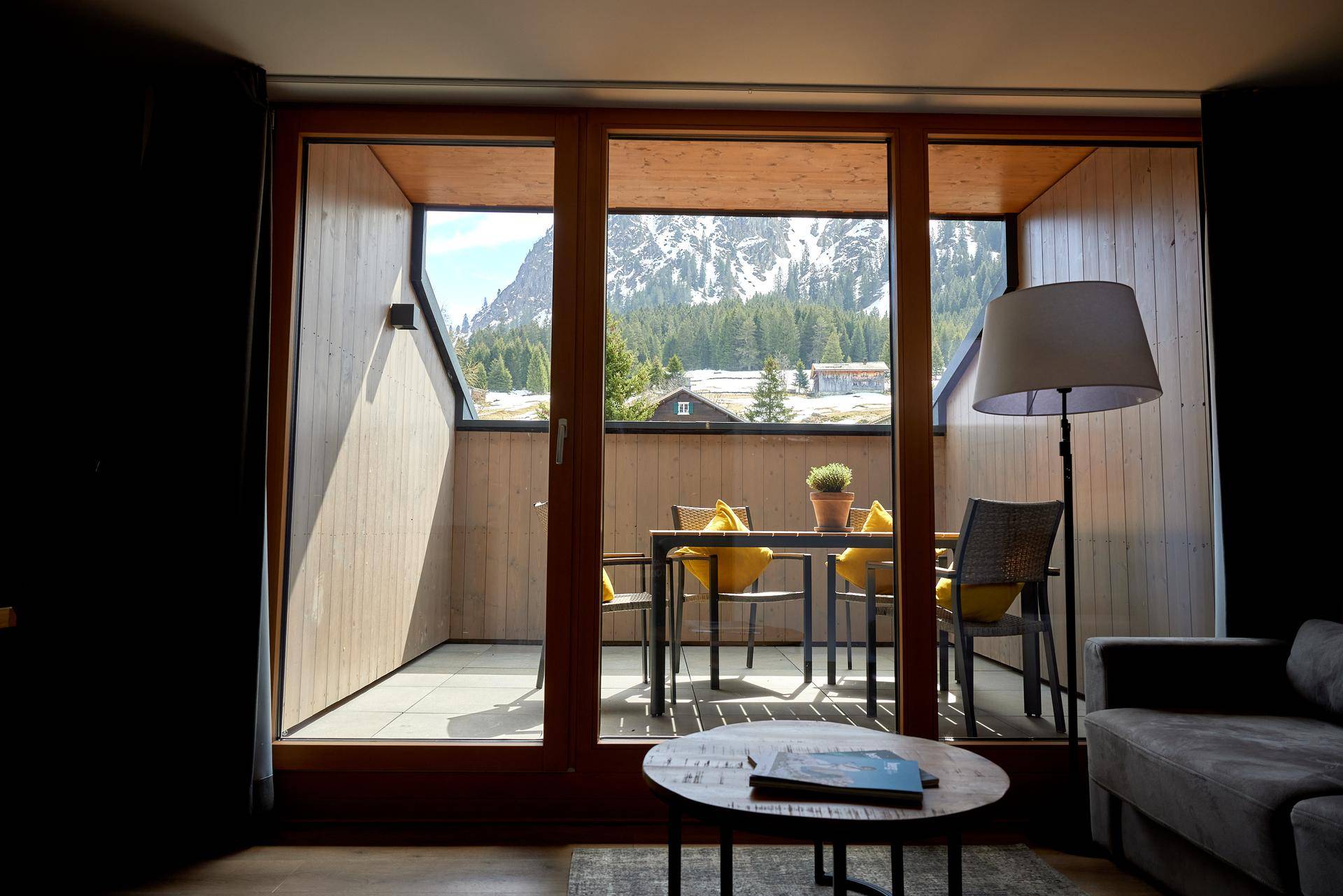 Gemütliches Wohnzimmer mit großen Fenstern und direktem Zugang zu einem Balkon mit Bergblick.