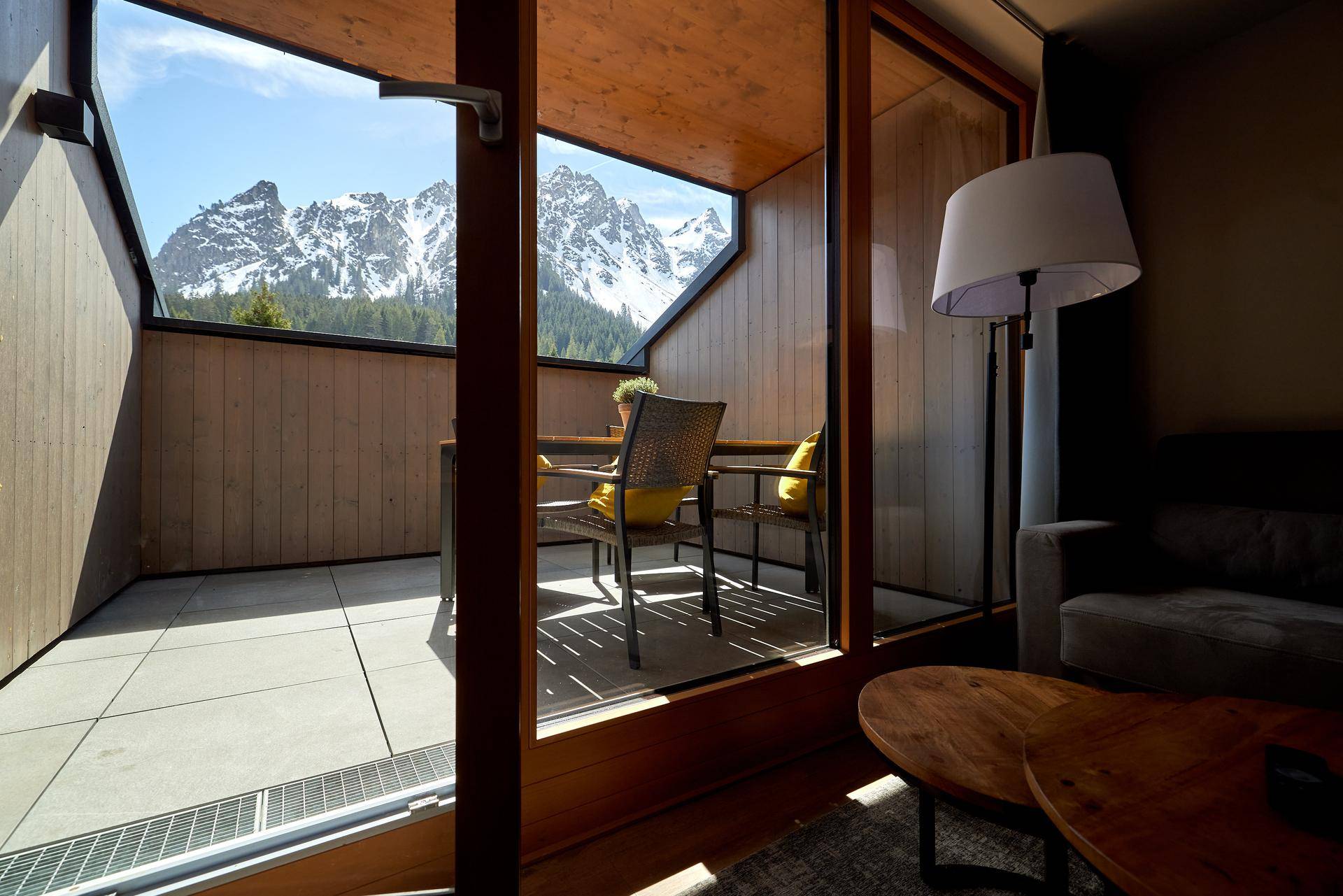 Wohnbereich mit großen Fenstern und direktem Zugang zum Balkon, der eine beeindruckende Bergkulisse bietet.