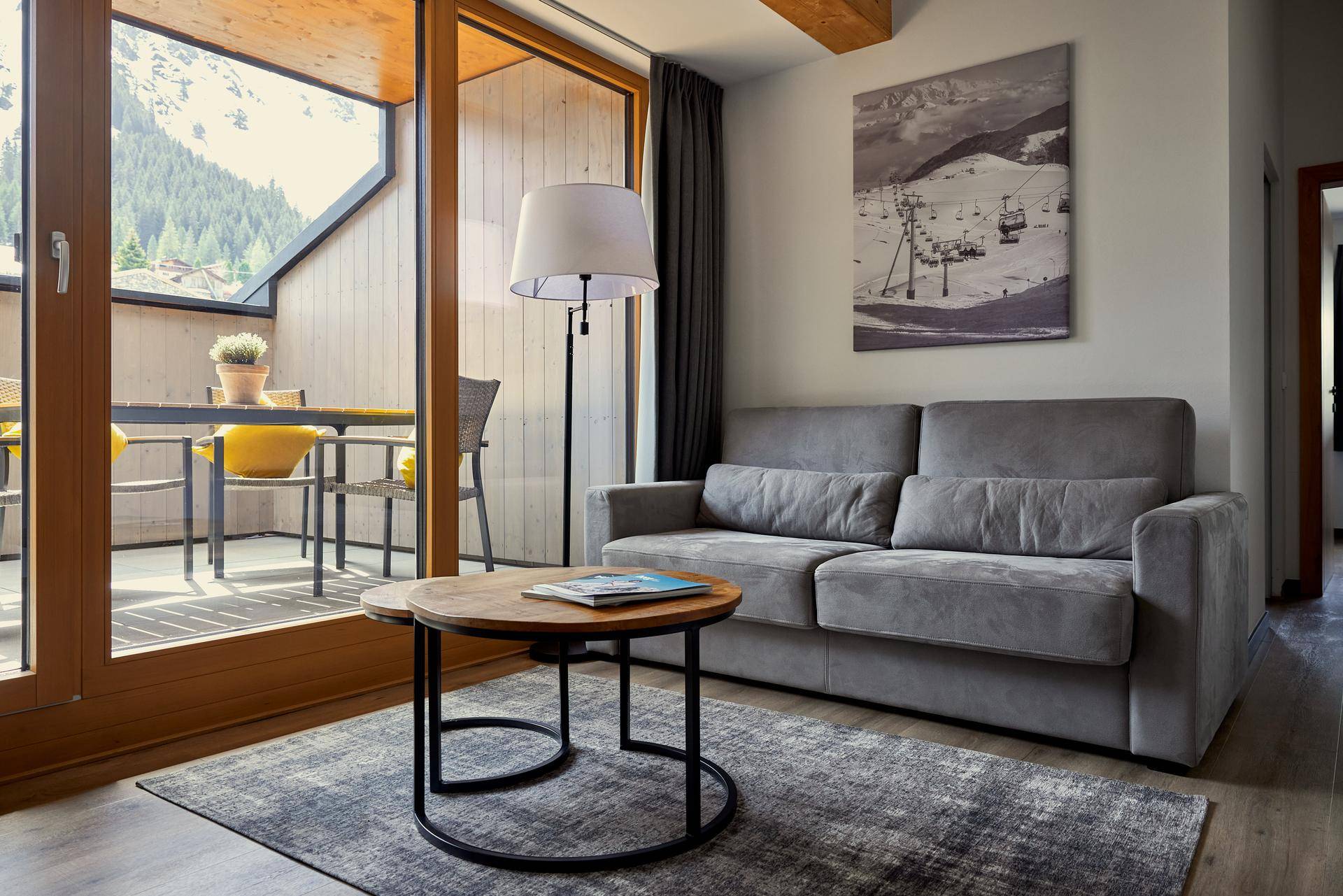 Gemütliches Wohnzimmer mit grauem Sofa, Teppich und Blick auf den Balkon mit Bergsicht.