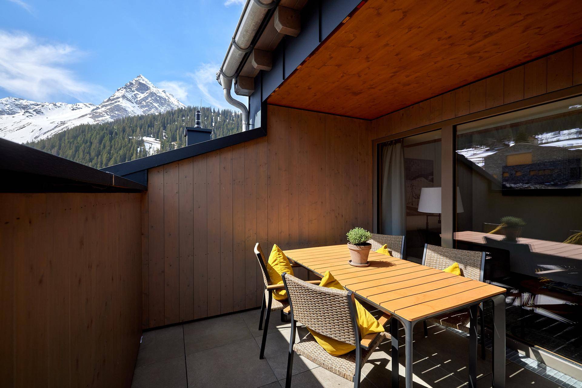 Sonniger Balkon mit Esstisch und Stühlen, umgeben von einer beeindruckenden Bergkulisse.