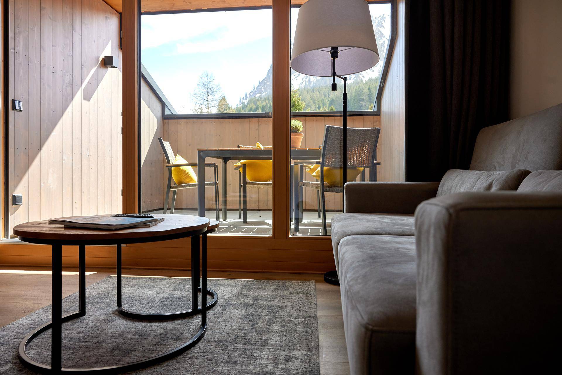 Heller Wohnbereich mit bequemer Couch und Blick auf den möblierten Balkon und die Berge.