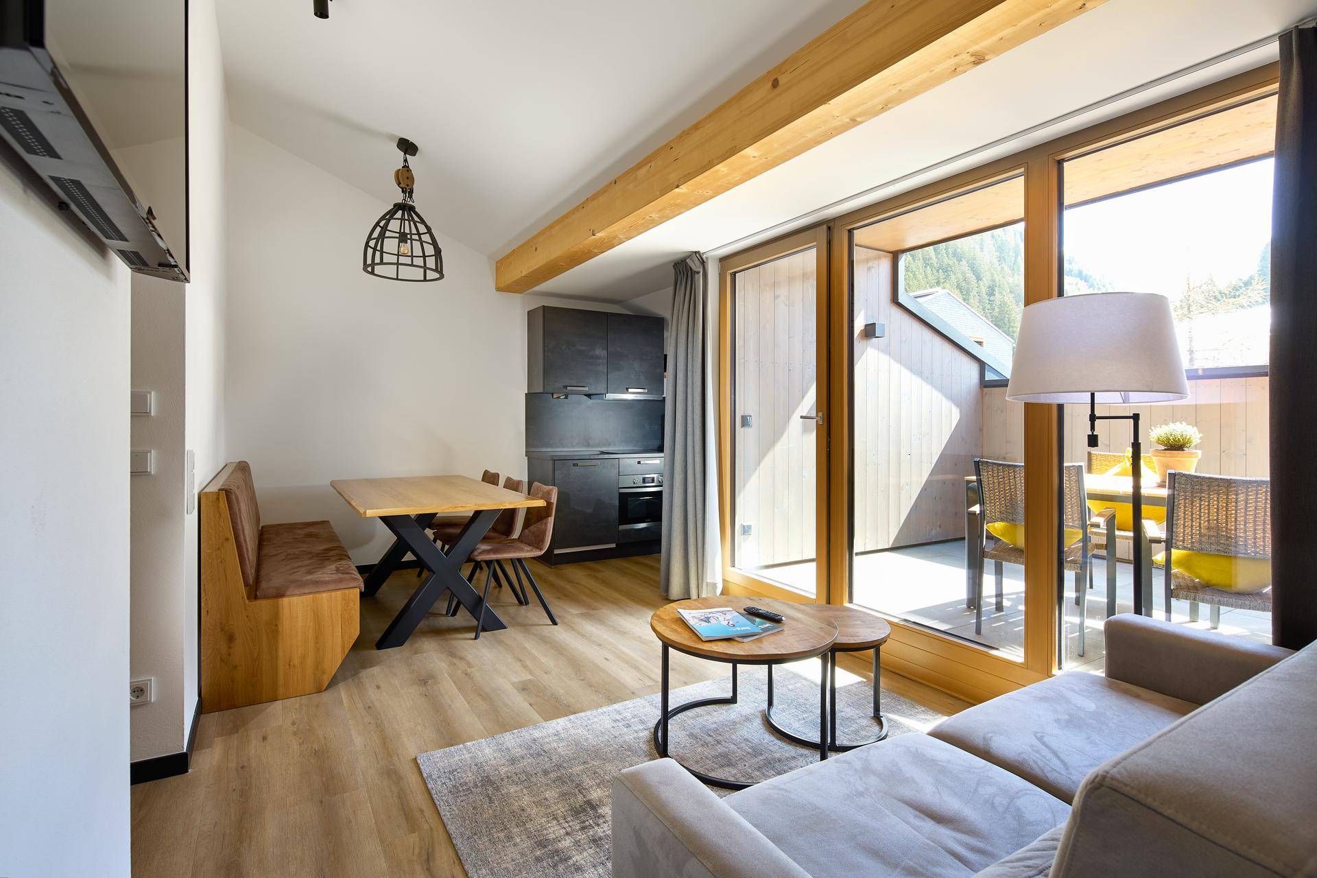 Gemütlicher Wohn-Essbereich mit integrierter Küchenzeile, Holzbalken und Zugang zum Balkon.