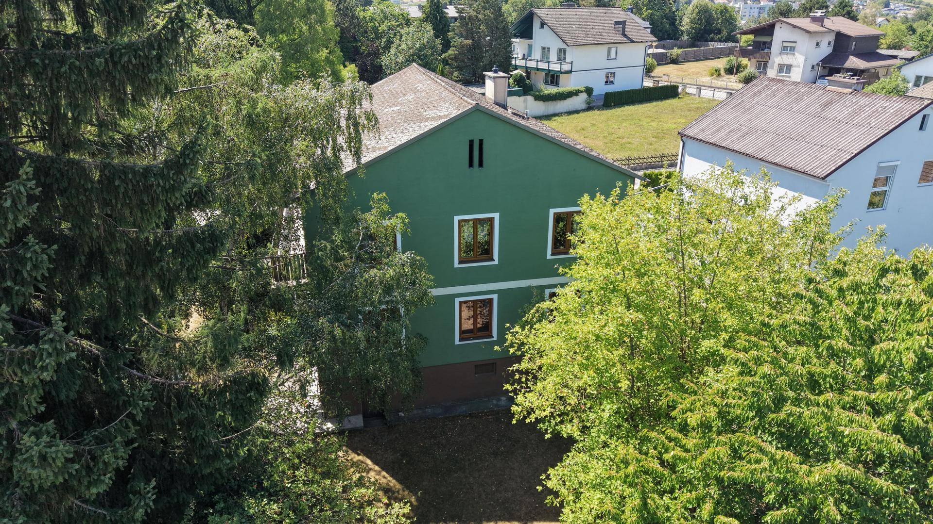 Luftaufnahme des Hauses mit grüner Fassade, umgeben von Bäumen und weiteren Wohnhäusern in der Nachbarschaft.
