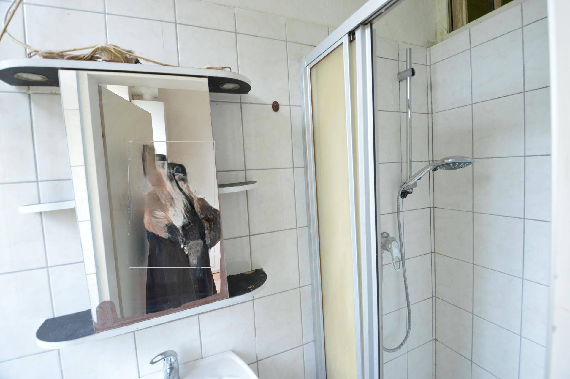 Badezimmer mit weiß gefliesten Wänden, Duschkabine und Spiegelschrank.