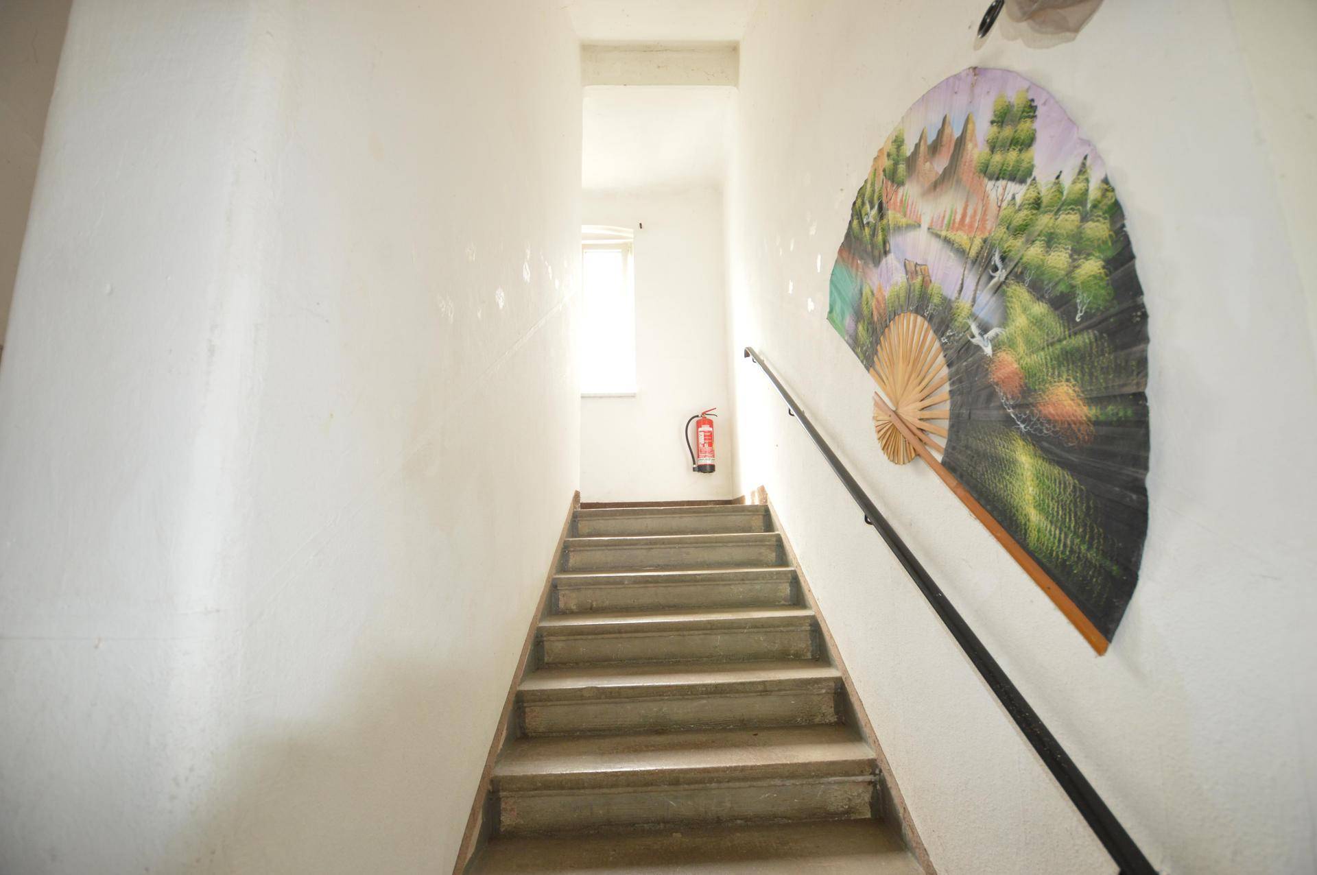 Treppenhaus mit weiß gestrichenen Wänden, Handlauf und einem dekorativen Fächer an der Wand.