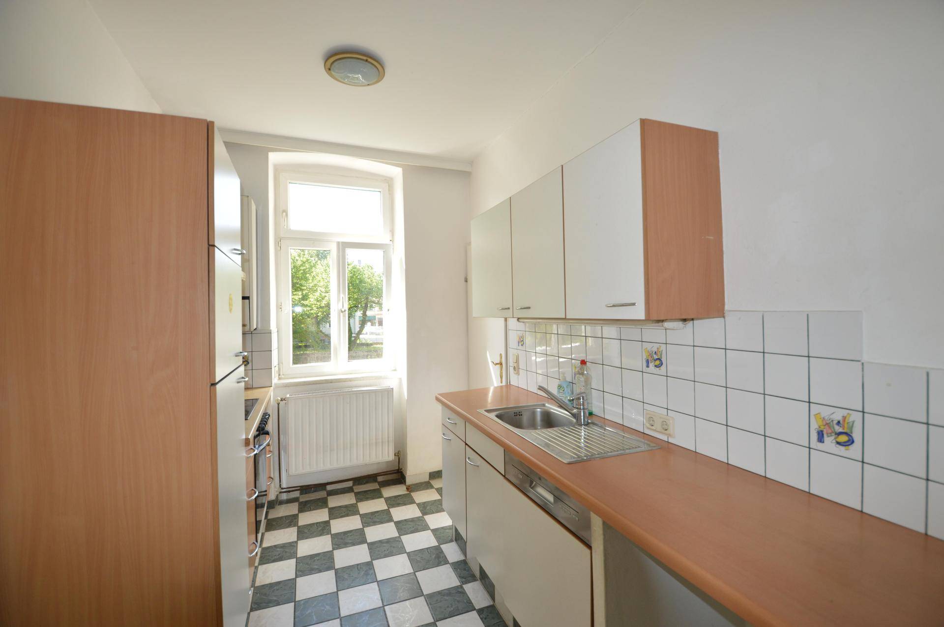 Helle Küche mit kariertem Fliesenboden, weißen Schränken und Fensterblick ins Grüne.