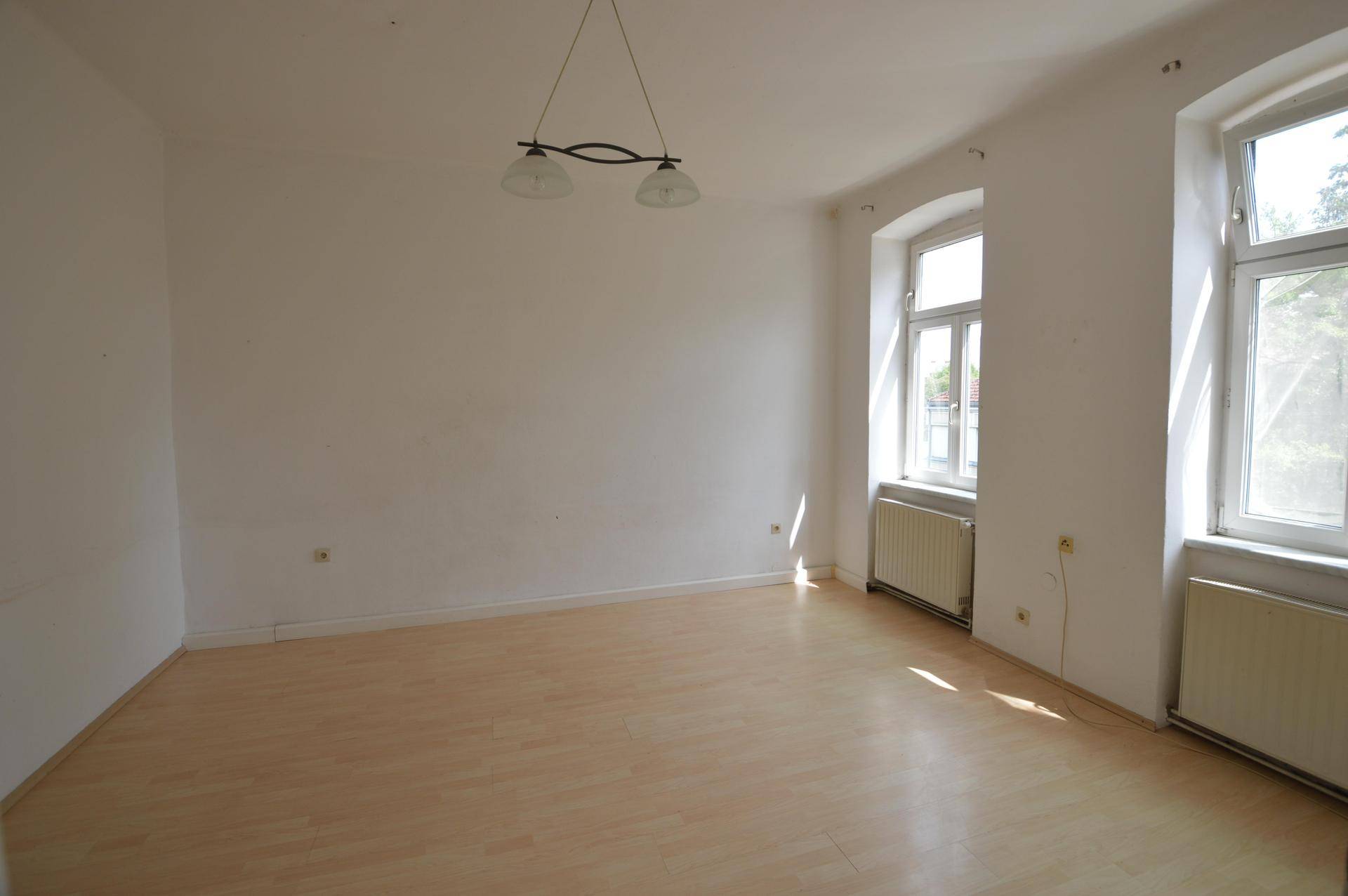 Heller Wohnraum mit Laminatboden, weißen Wänden und zwei großen Fenstern.