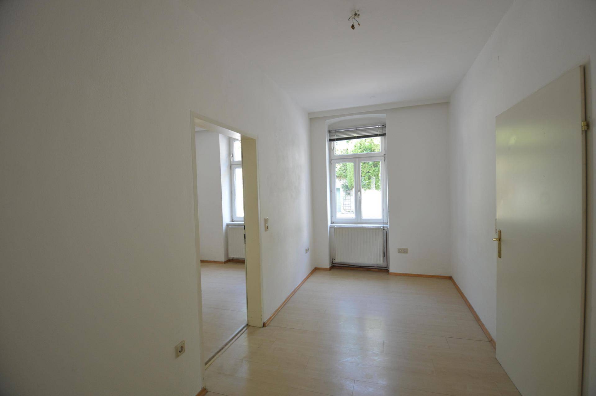Geräumiges Zimmer mit Laminatboden, weiß gestrichenen Wänden und Fenster mit Blick nach draußen.