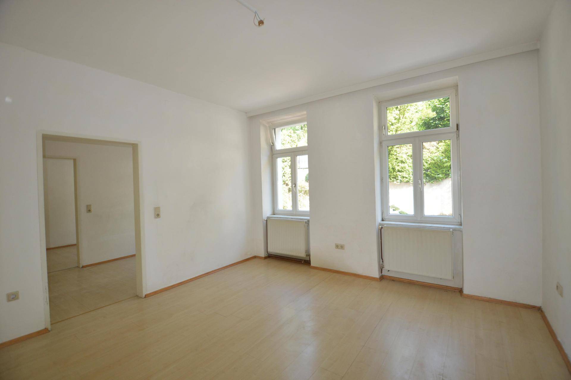 Heller Wohnraum mit Laminatboden, weißen Wänden und Zugang zu einem weiteren Zimmer.