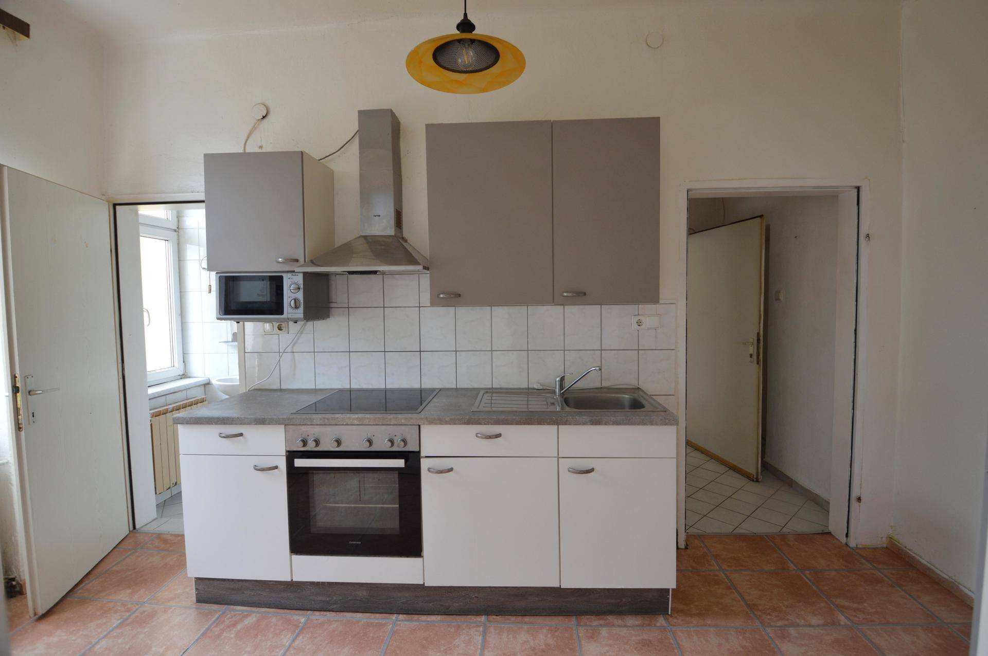 Funktionale Küche mit Terrakotta-Fliesenboden, Einbaugeräten und einem Fenster für Tageslicht.