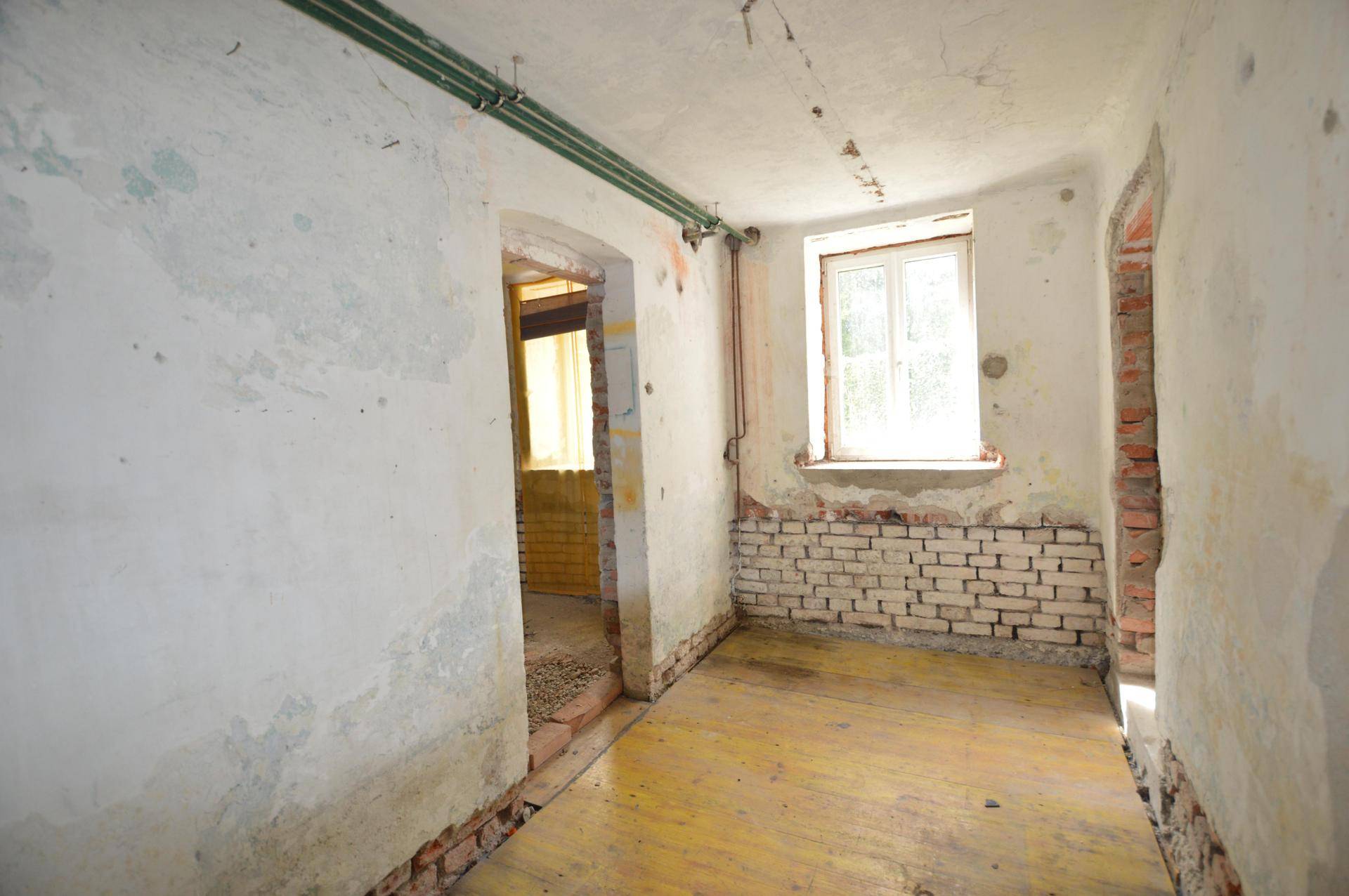 Raum in sanierungsbedürftigem Zustand mit freigelegten Ziegelwänden und Holzboden.