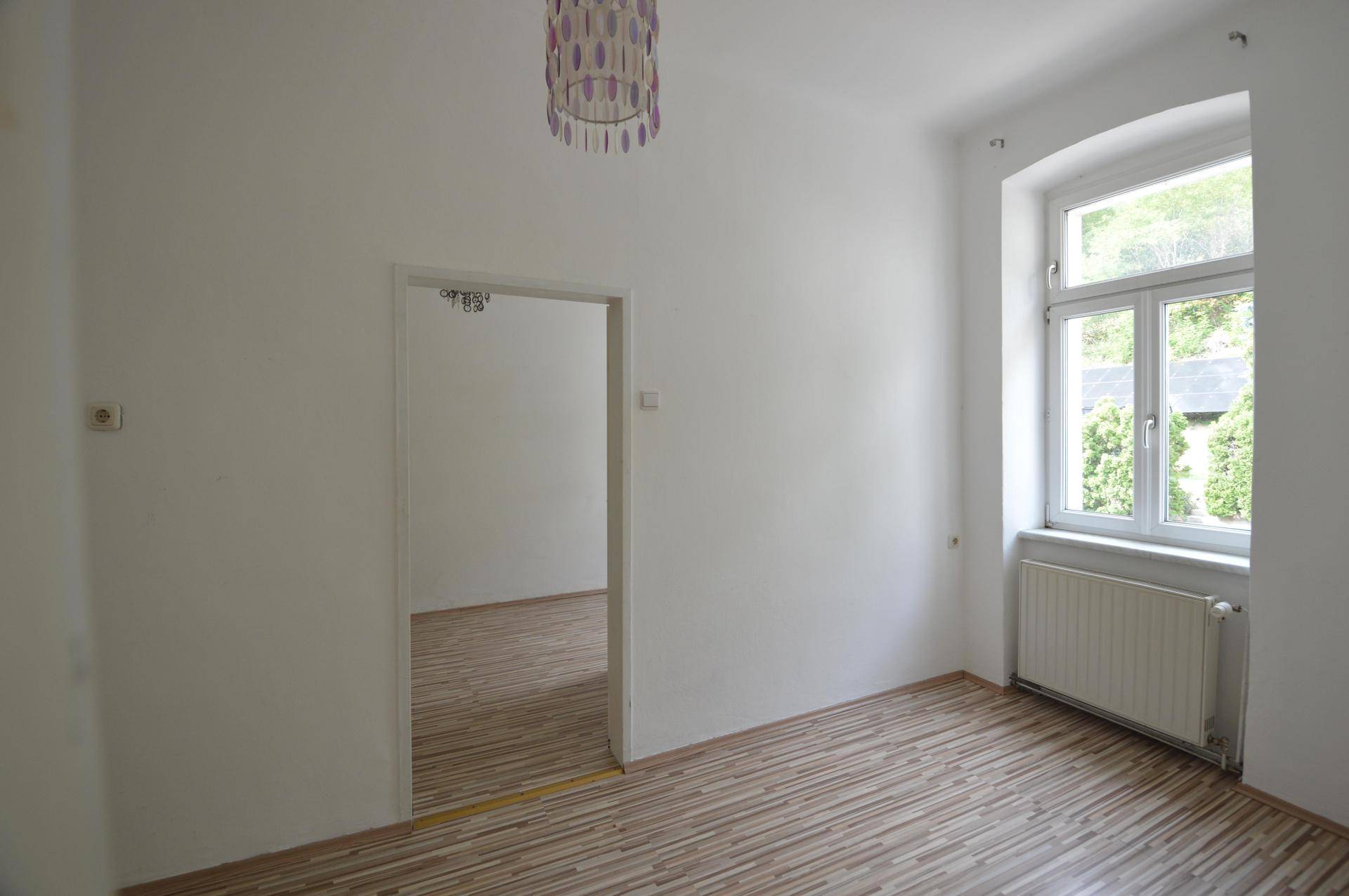 Helles Schlafzimmer mit Laminatboden, weiß gestrichenen Wänden und einem Fenster.