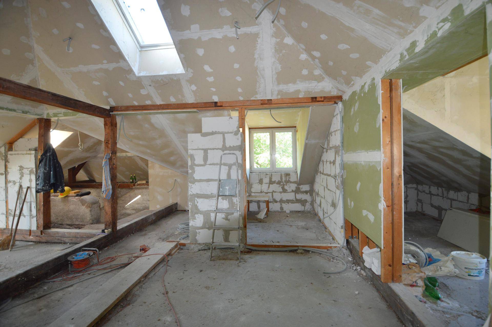 Dachgeschoss im Rohbau mit Dachfenster und vorbereiteten Wänden für den Innenausbau.