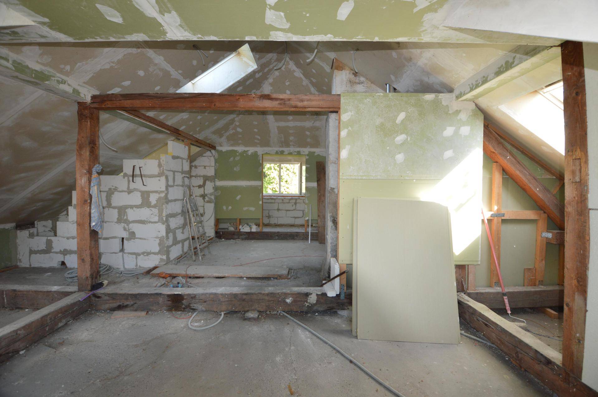 Dachgeschoss im Rohbau mit sichtbaren Holzbalken und Dachfenstern, bereit für den Ausbau.
