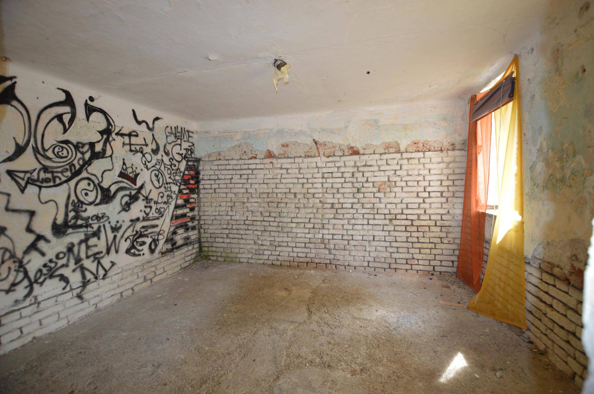 Sanierungsbedürftiger Raum mit Graffiti an den Wänden und freigelegten Ziegeln.