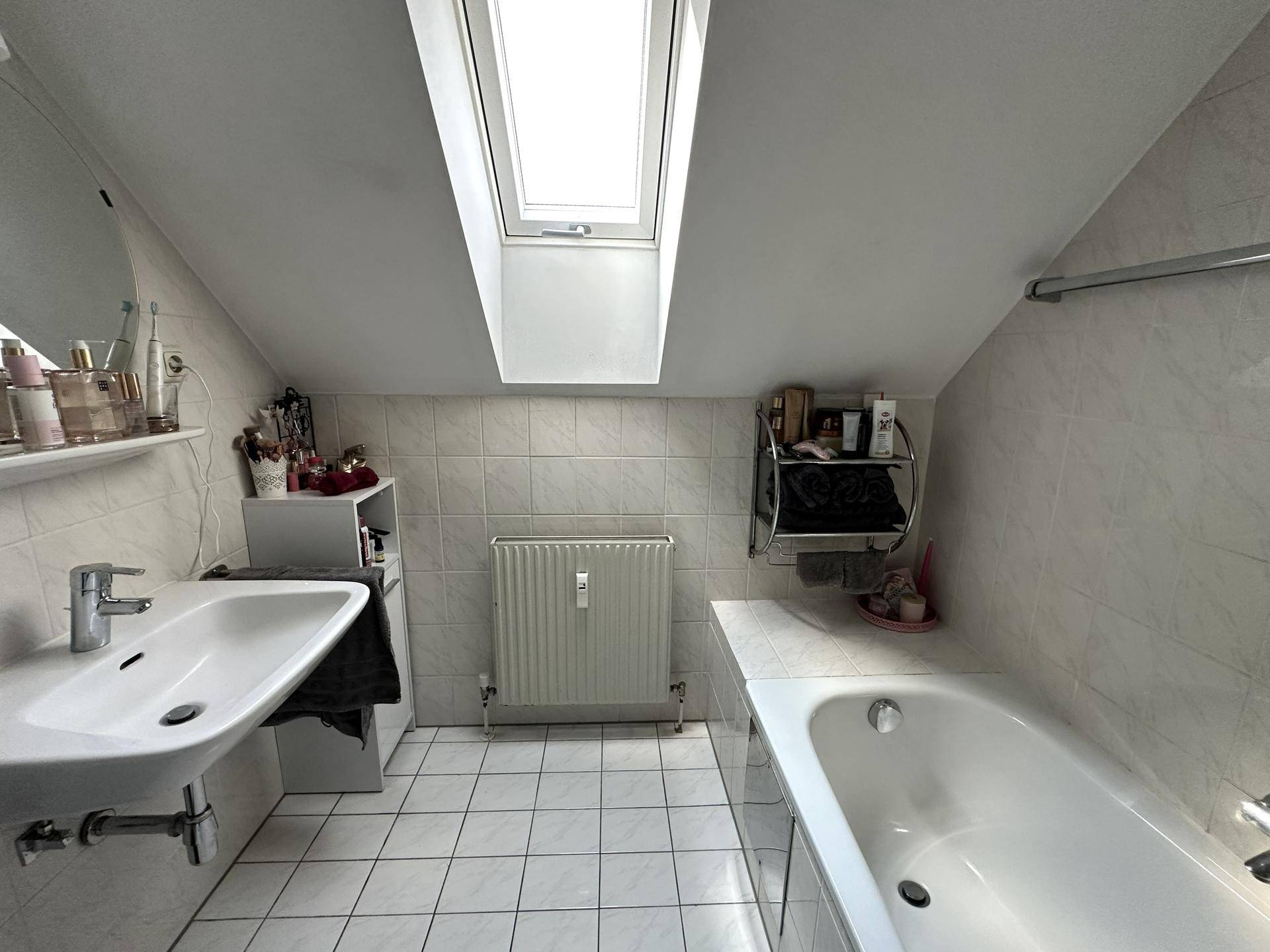 Badezimmer im Dachgeschoss mit Badewanne, Waschbecken und Dachfenster für Tageslicht.