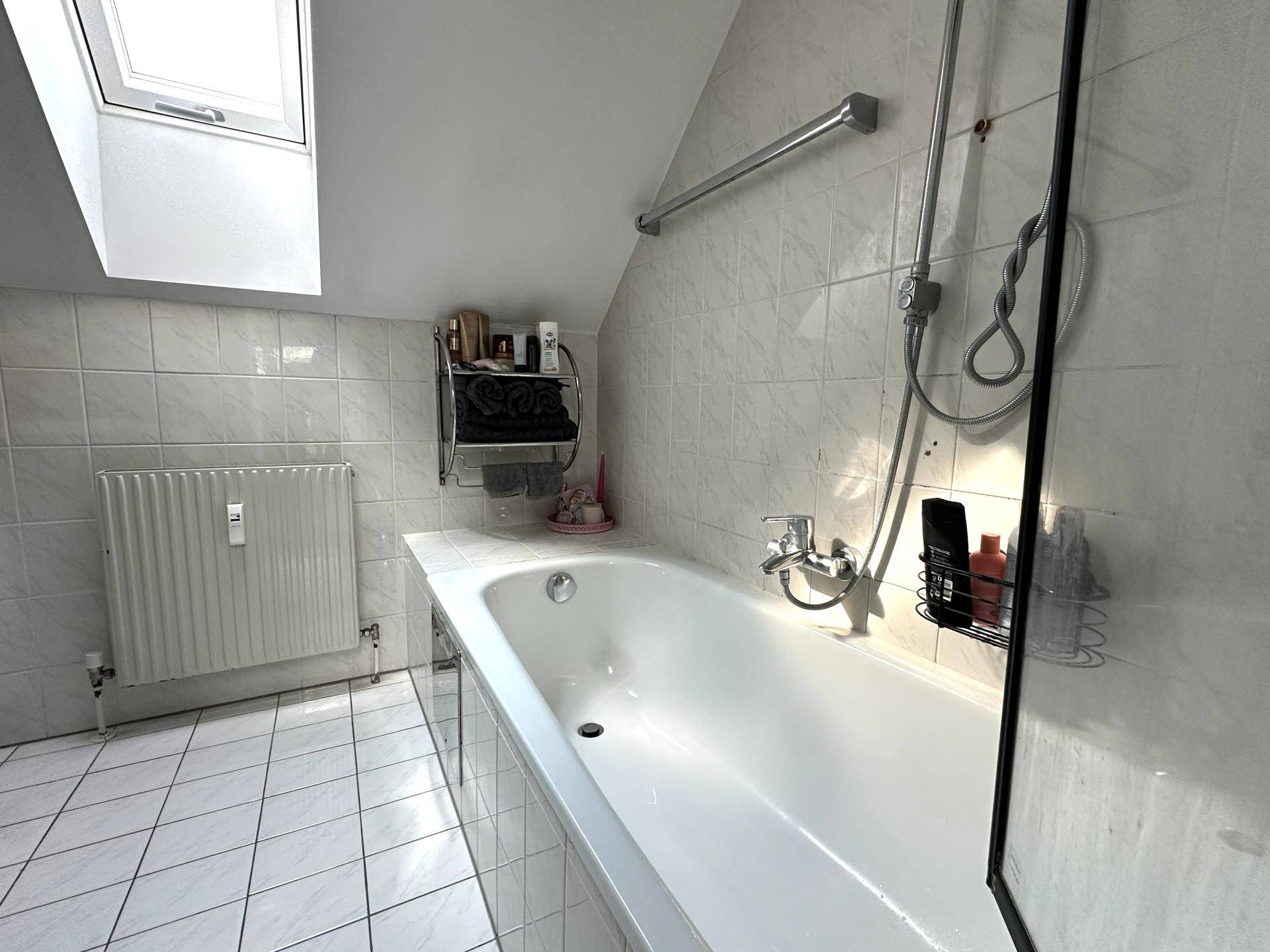 Gefliestes Badezimmer mit Badewanne und Duschvorrichtung im Dachgeschoss.