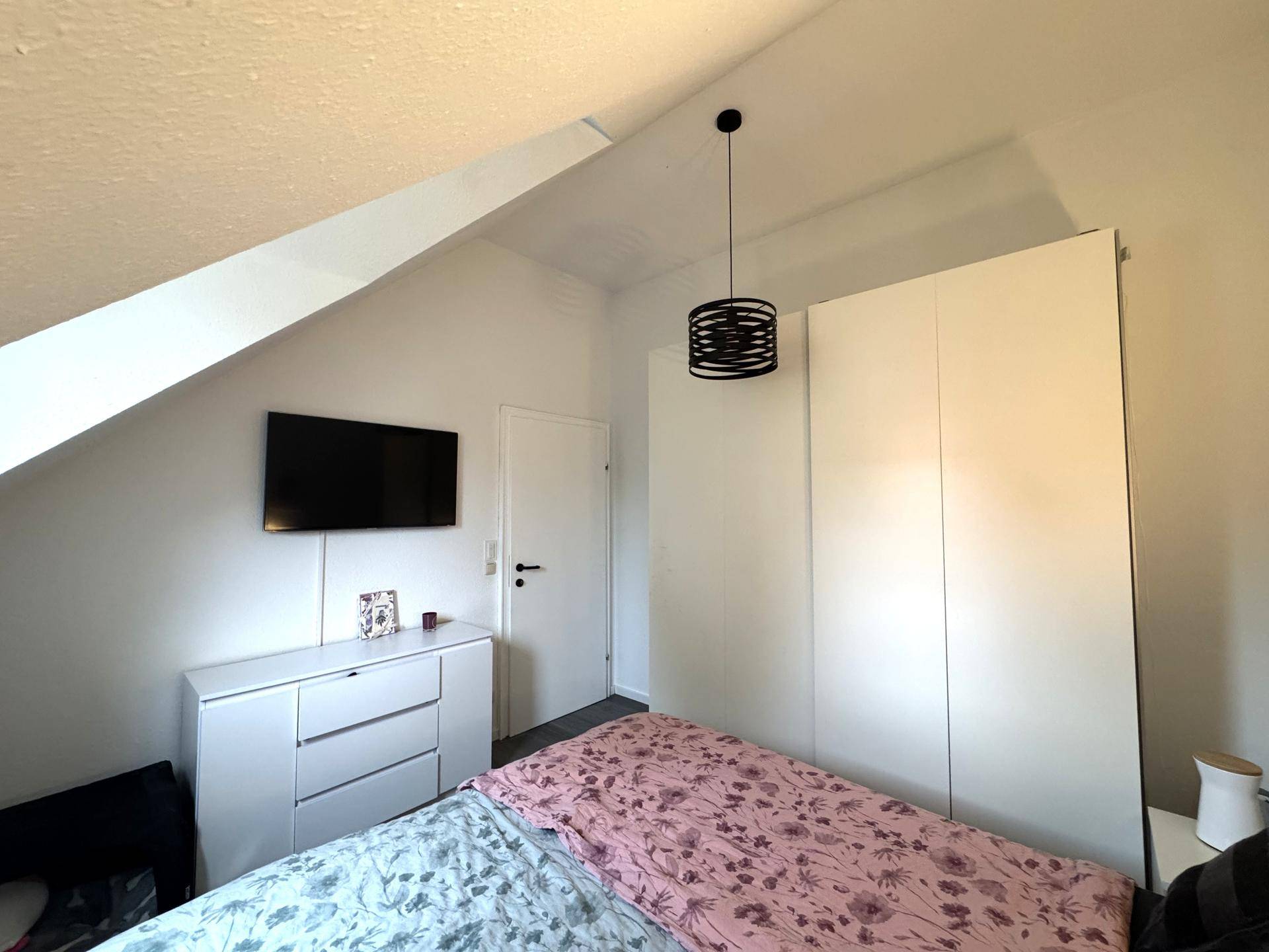 Helles Schlafzimmer mit Kleiderschrank, Kommode und schrägen Wänden im Dachgeschoss.