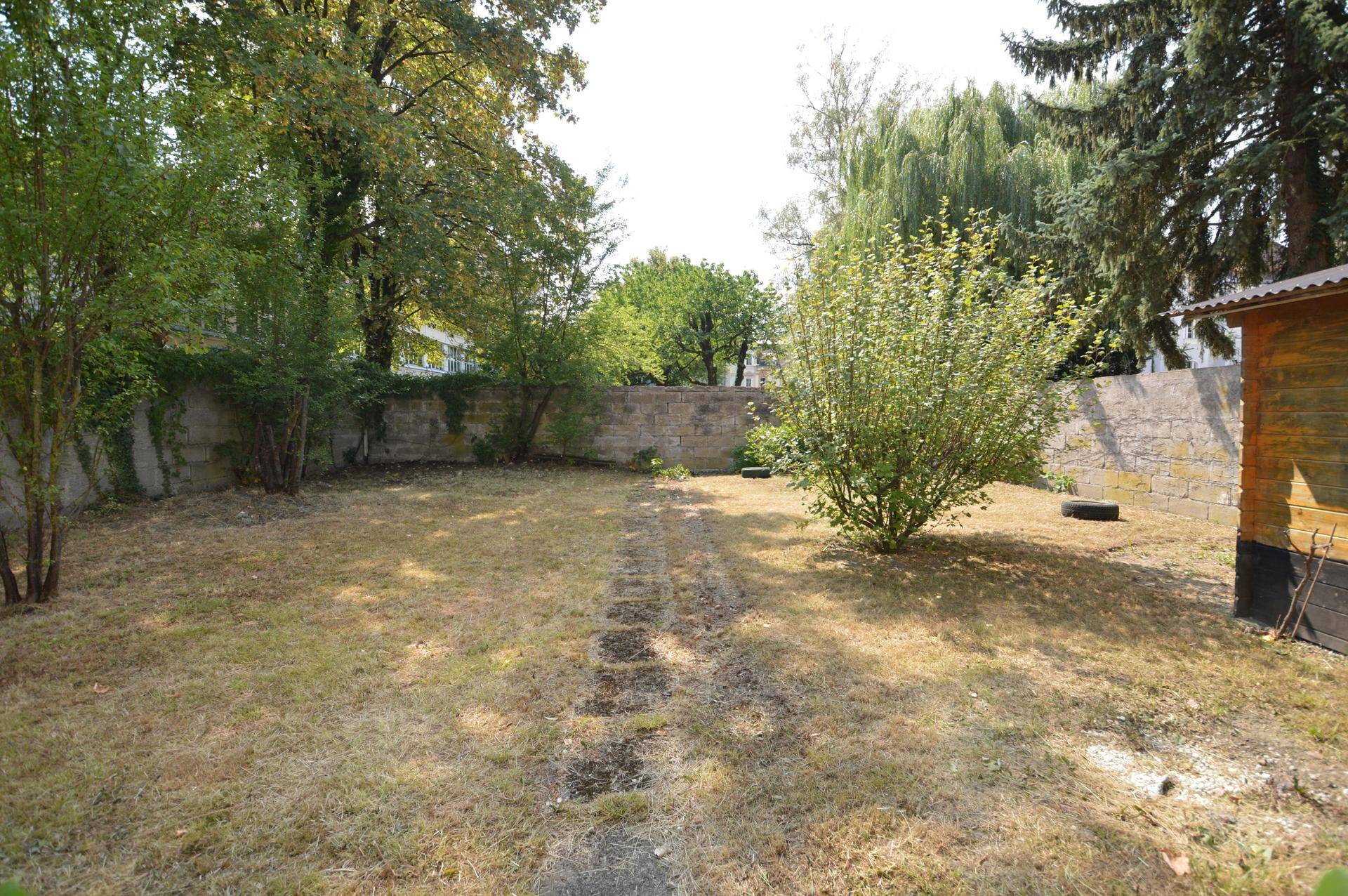 Großer Gartenbereich mit Rasenfläche, Bäumen und einer Steinmauer im Hintergrund.