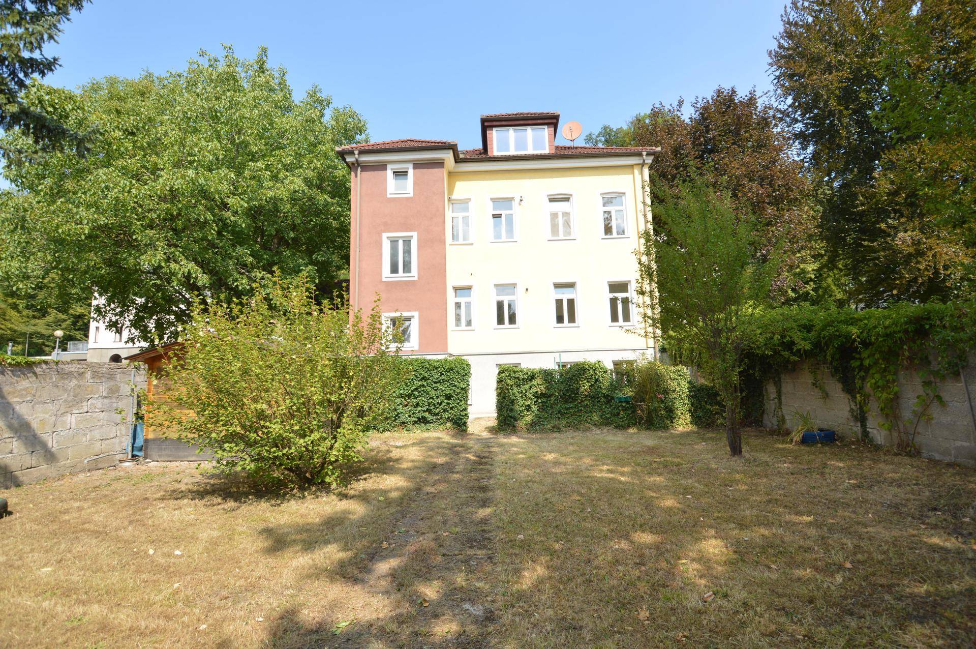 Garten mit Rasenfläche und Blick auf das gelbe Mehrfamilienhaus mit grüner Hecke.