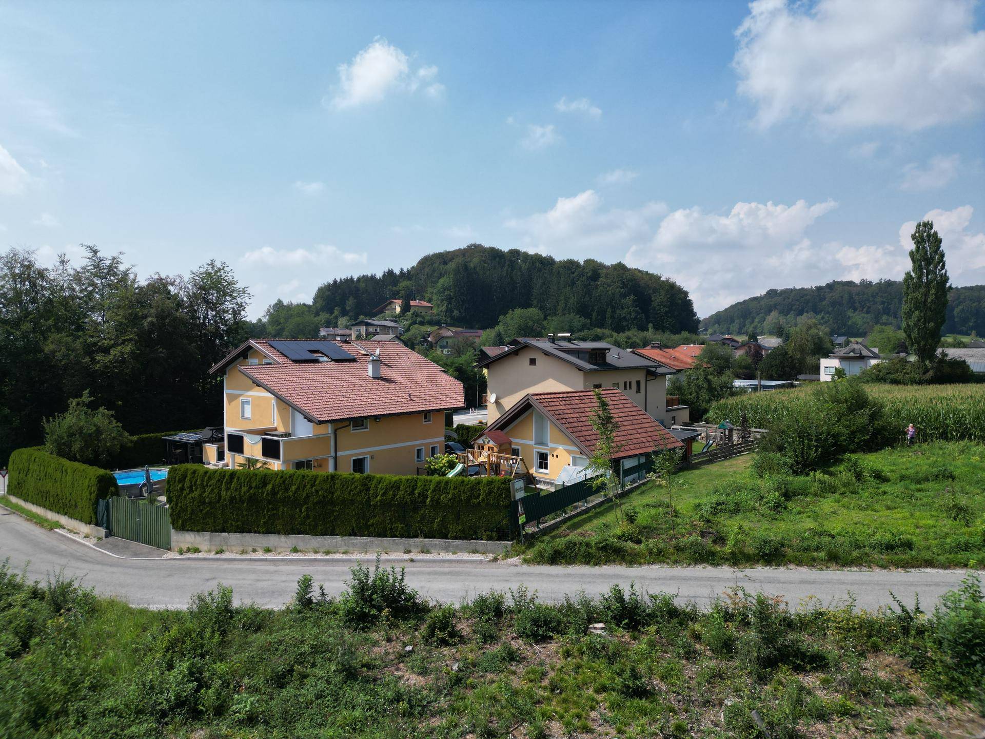 Mehrere Wohnhäuser in ländlicher Umgebung mit grünen Hügeln und Feldern im Hintergrund.