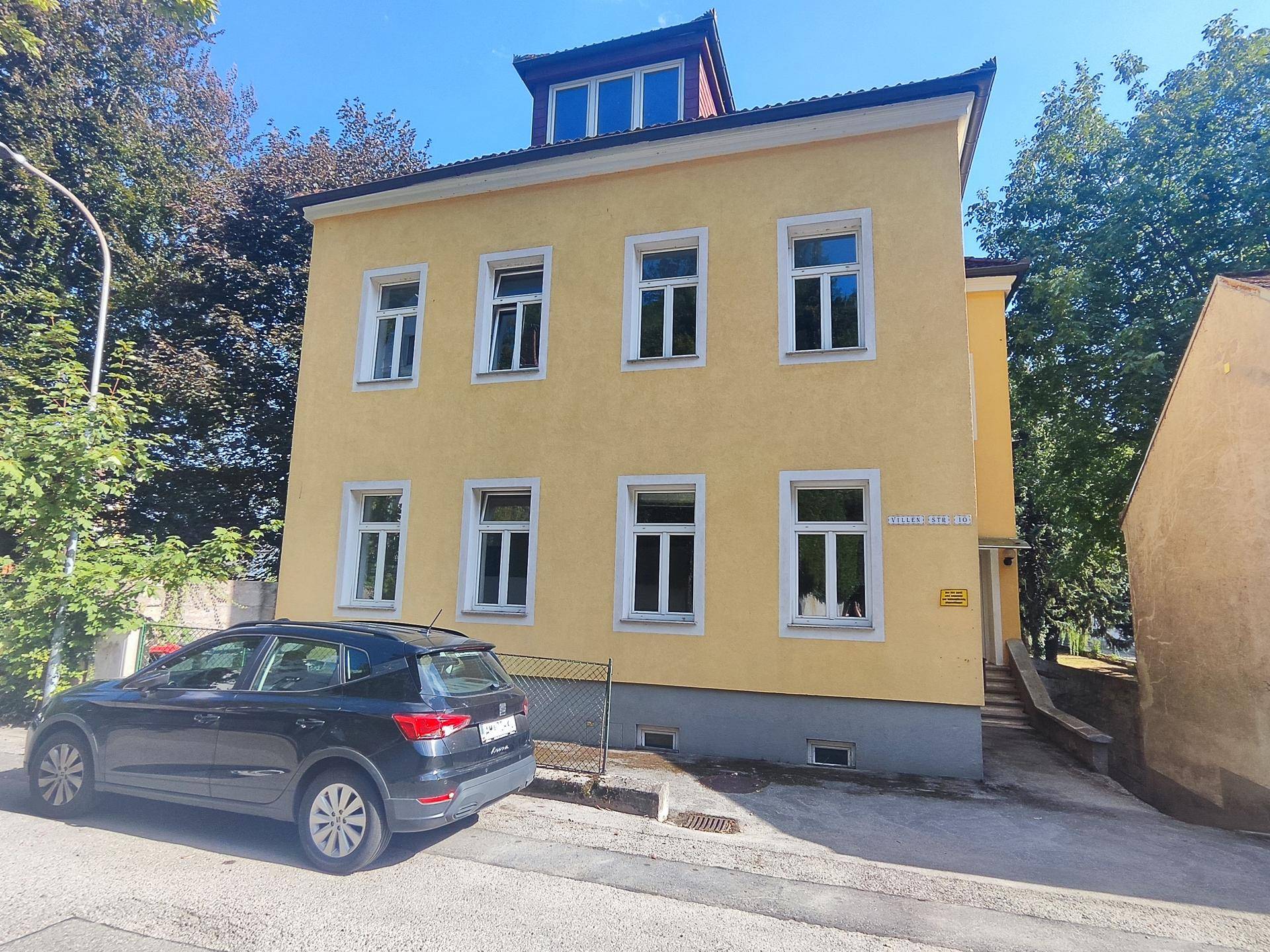 Gelbes Wohnhaus mit weißem Dachgeschoss und parkendem Auto auf der Straße.