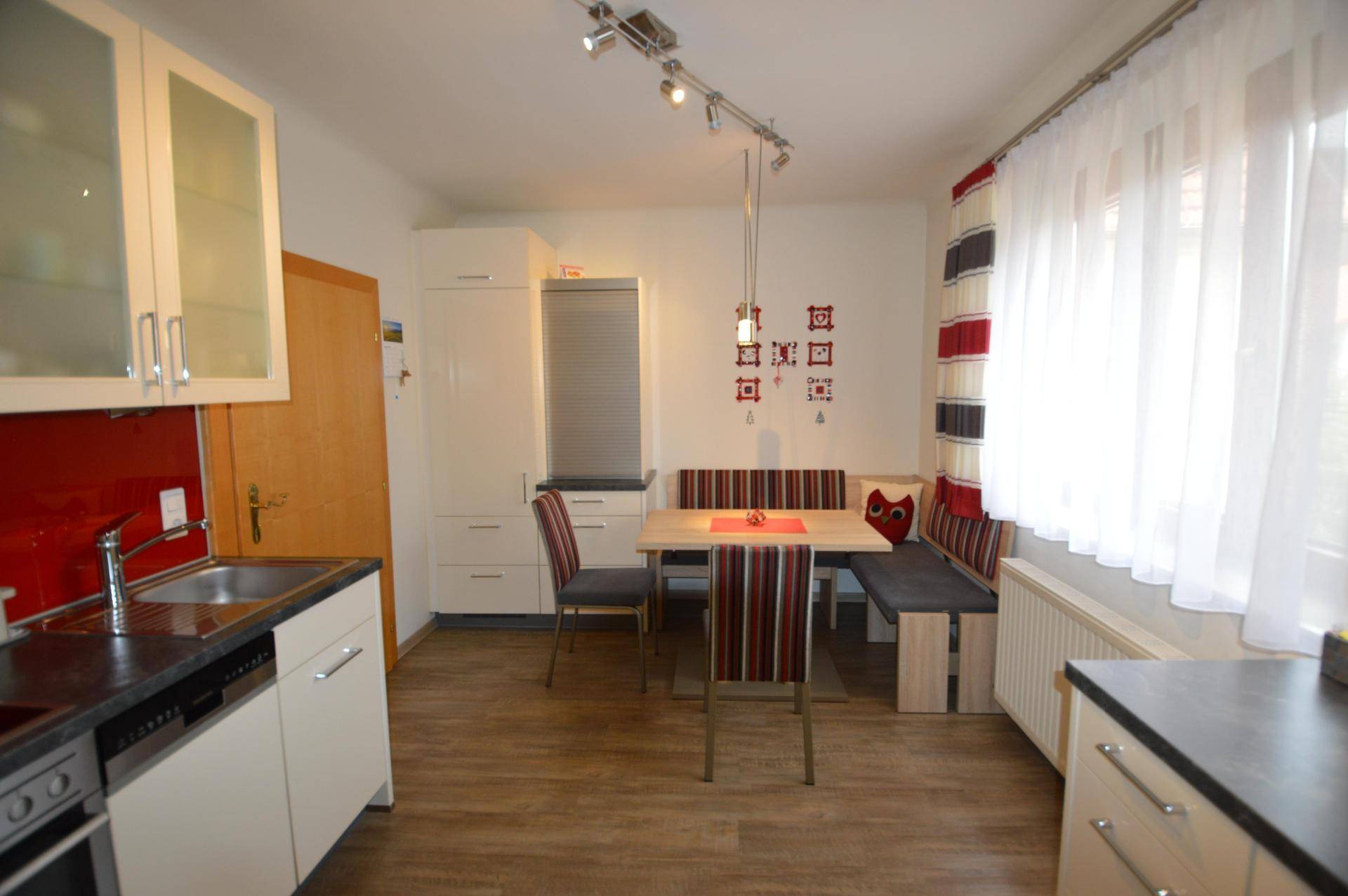 Gemütliche Küche mit Essbereich, weißen Schränken, Holzboden und roten Akzenten.