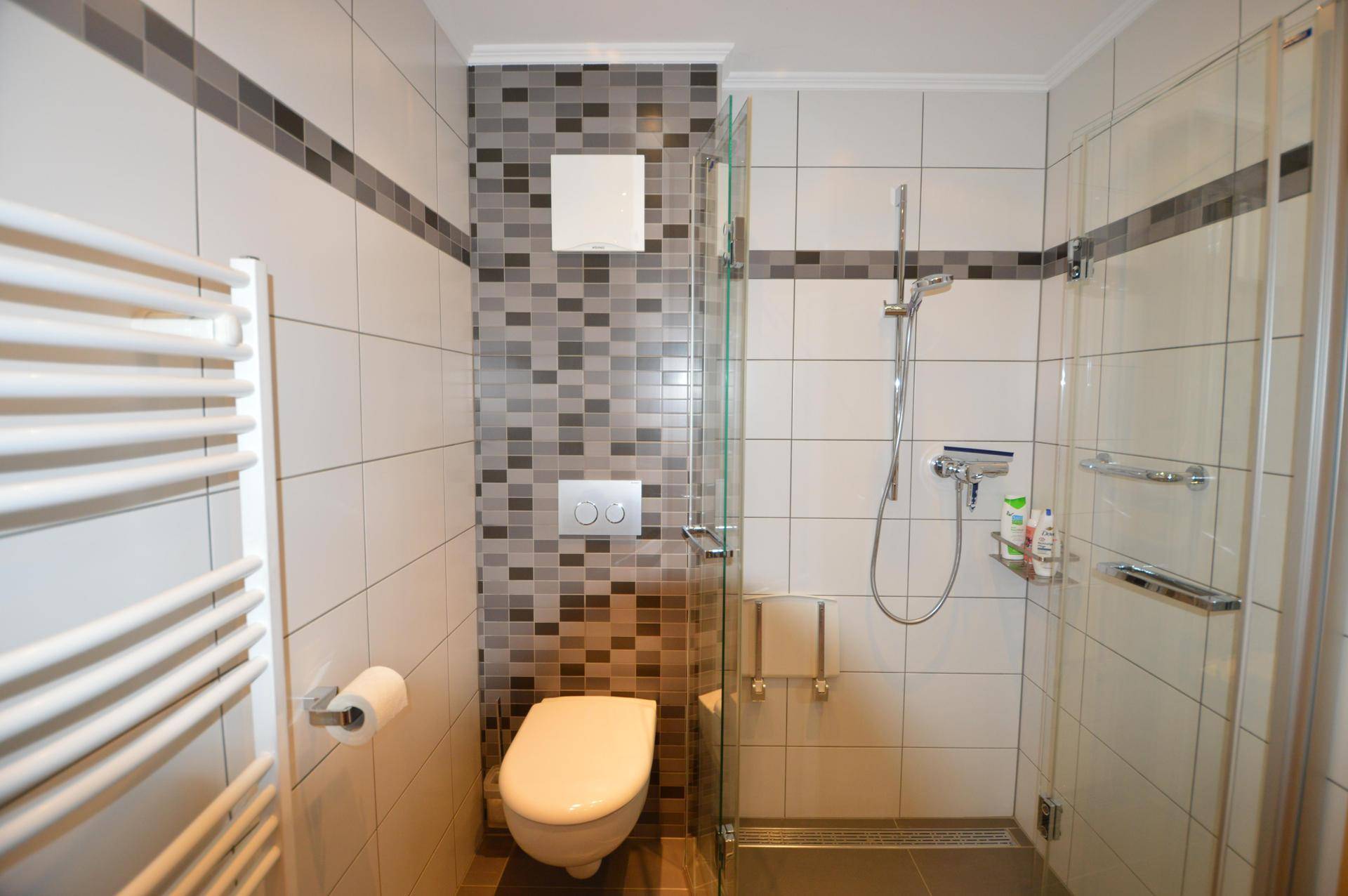 Badezimmer mit Duschkabine, wandhängendem WC und modernen Fliesen in Grau- und Weißtönen.