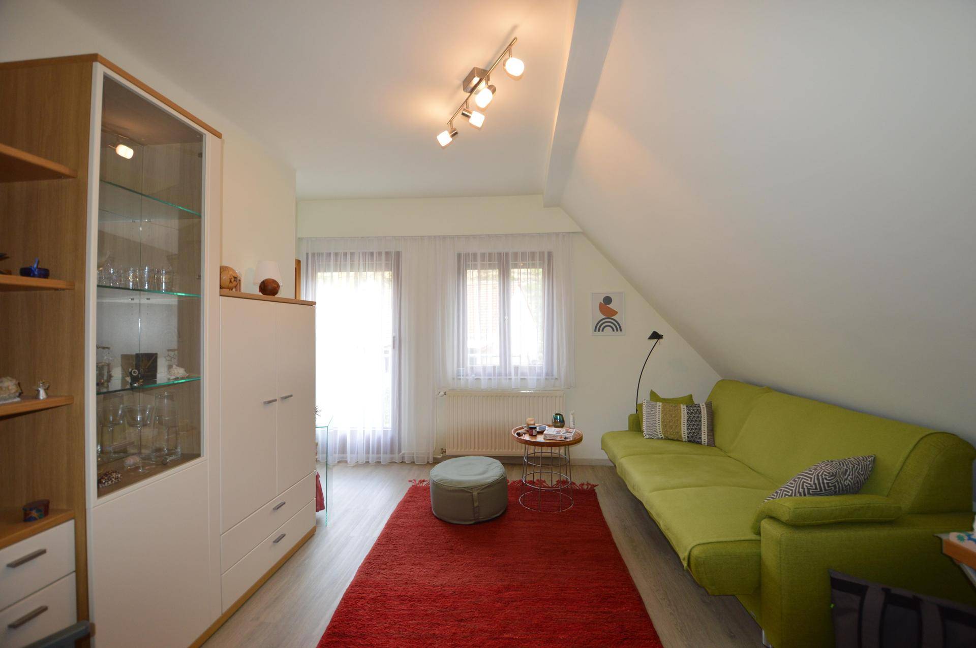 Helles Wohnzimmer im Dachgeschoss mit grünem Sofa, rotem Teppich und Dachschräge.