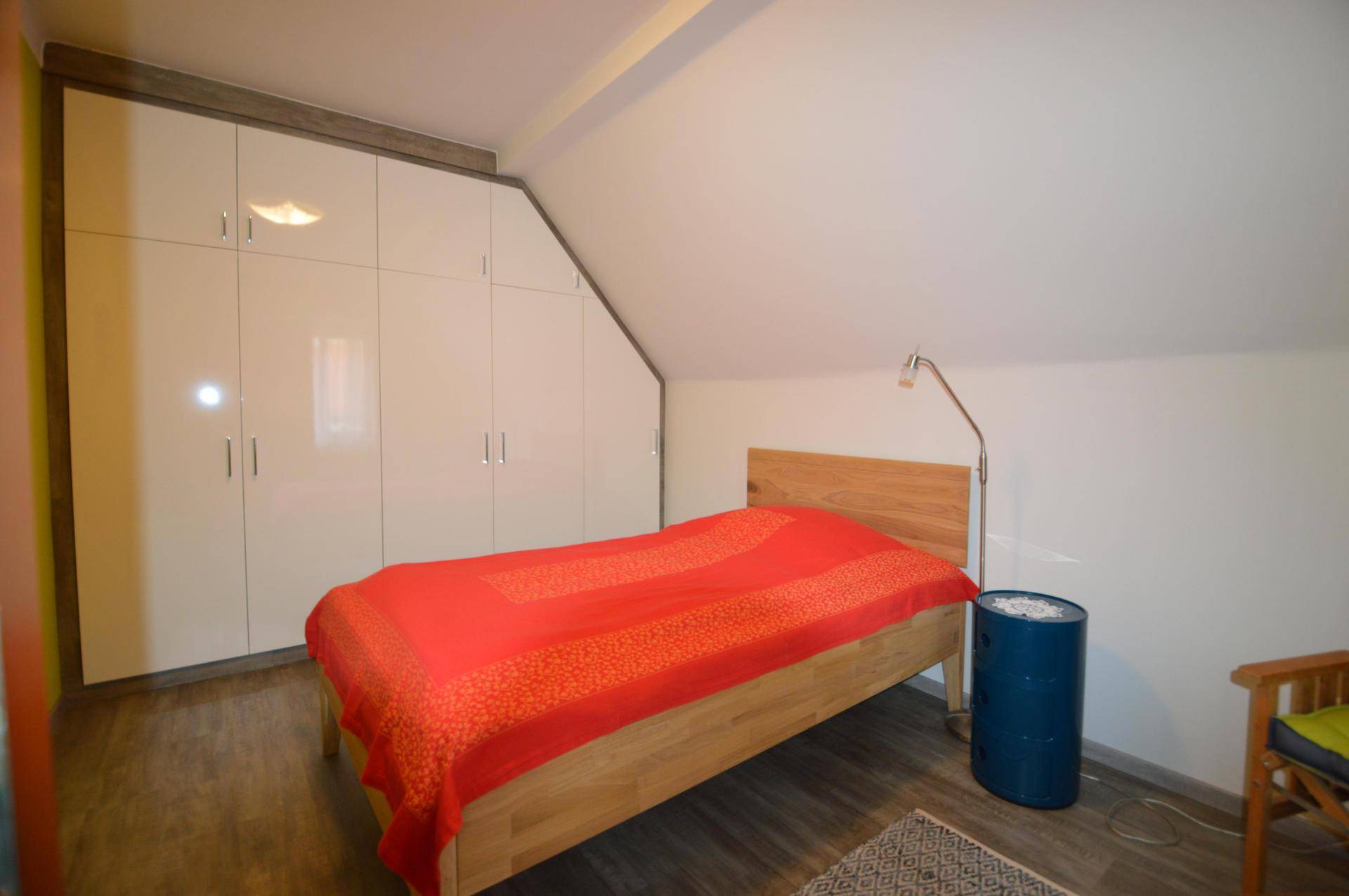 Schlafzimmer im Dachgeschoss mit Holzbett, weißen Einbauschränken und Dachschräge.
